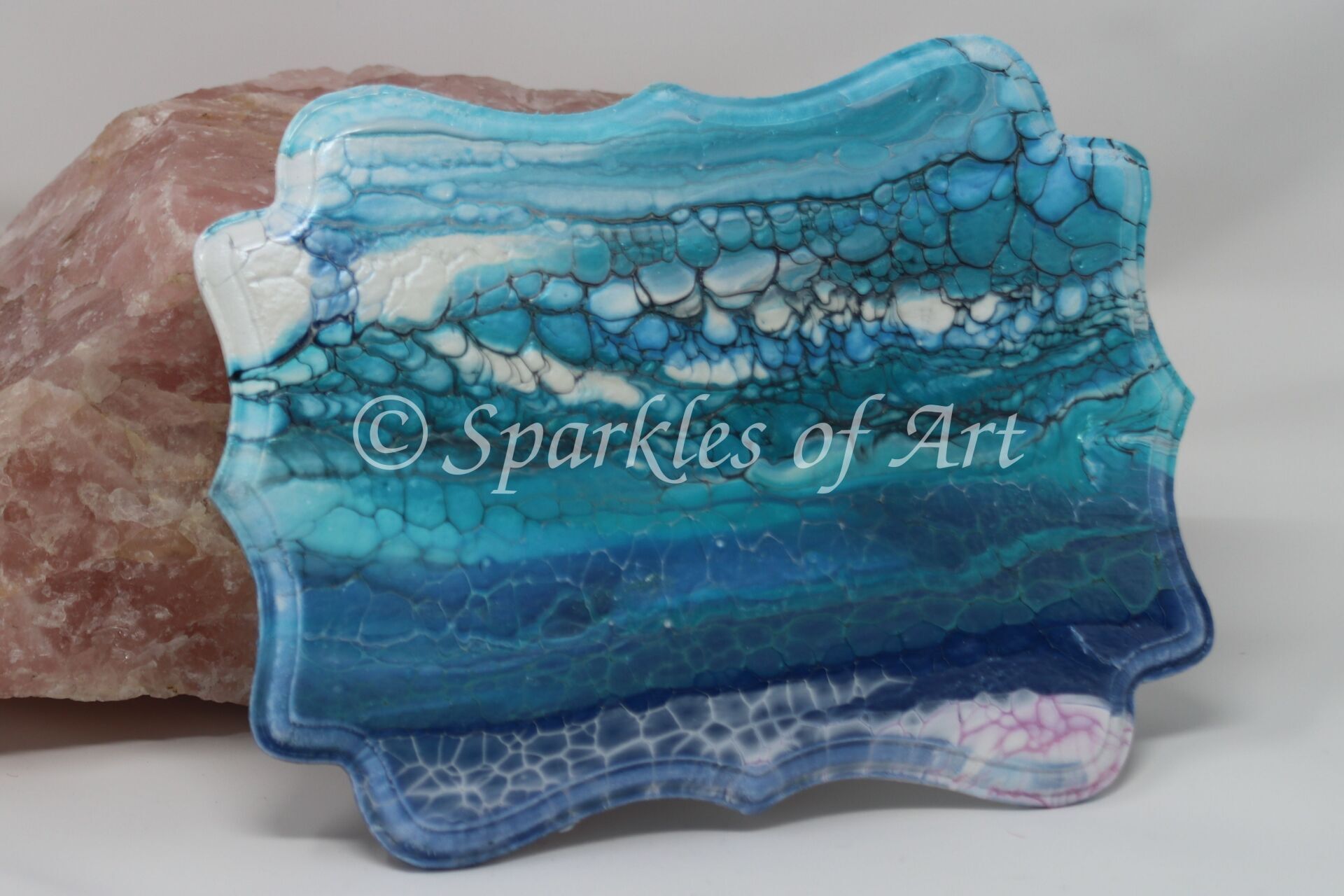 Blue translucent decorative glass plaque with bubble texture and wavy edges, resting on a stone base