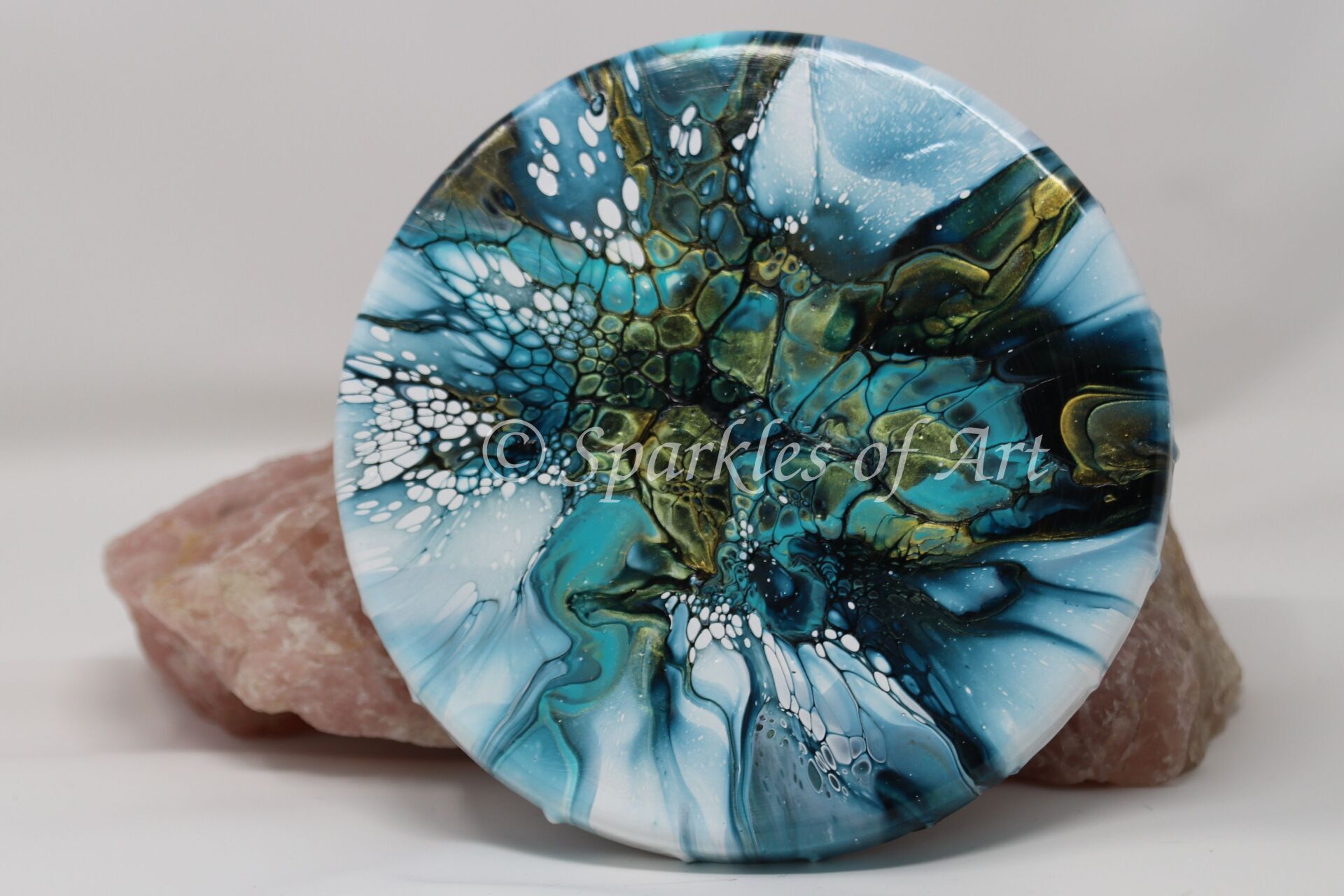 Round blue abstract art disc resting on a pink stone base
