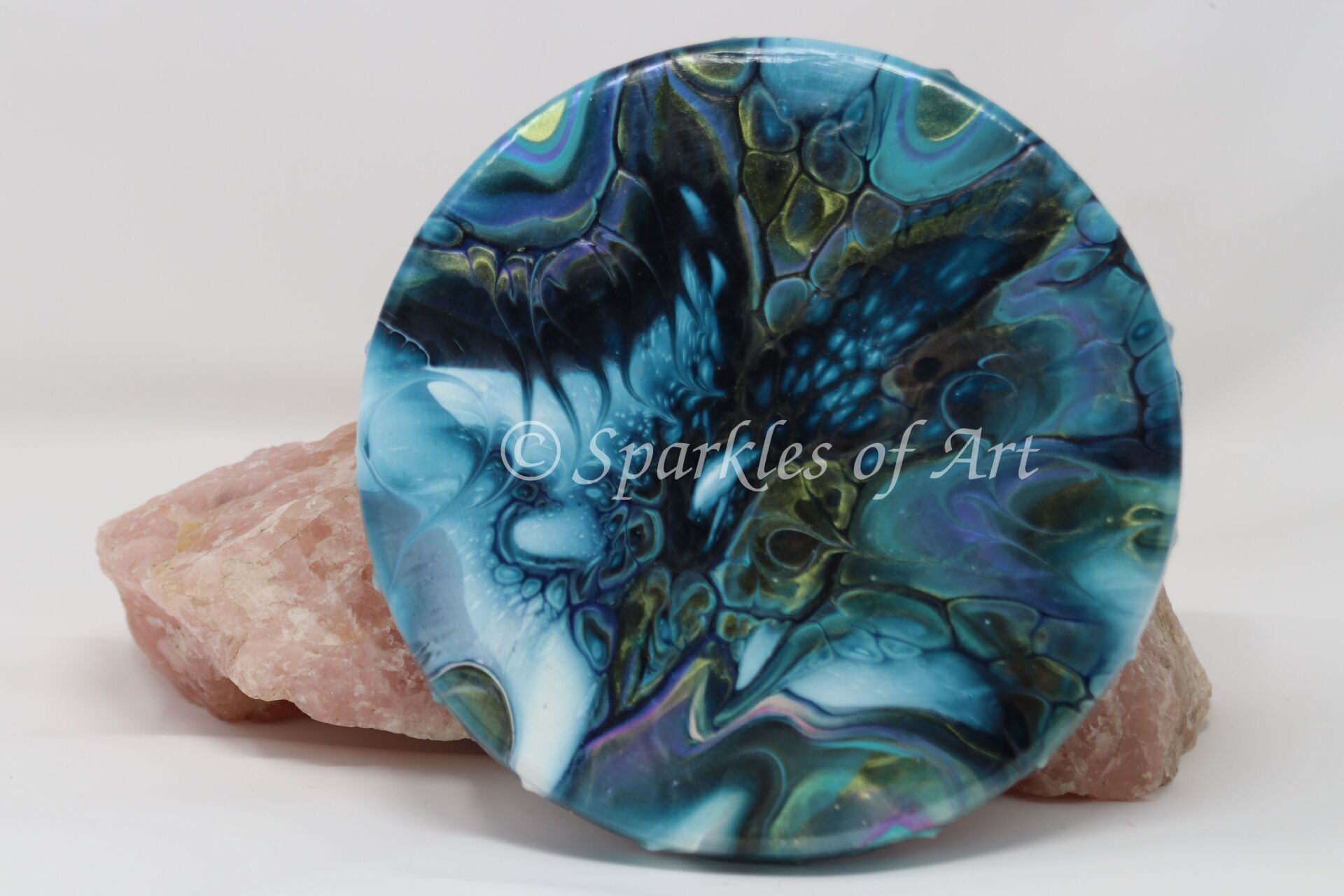 Blue abstract round art piece on pink stone, with “Spircles of Art” text