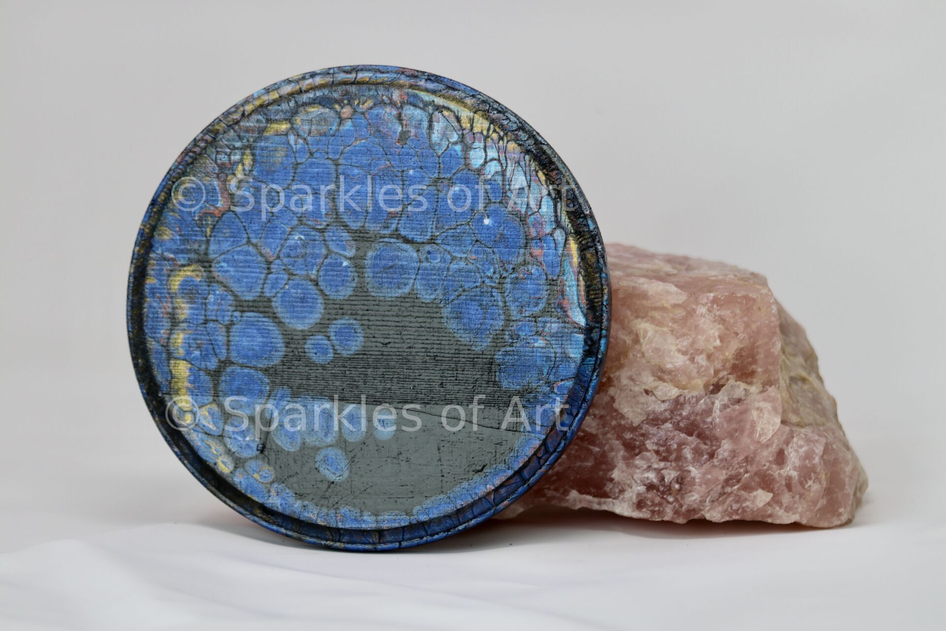 Blue sparkling mineral sphere on a pink rock base against a white background