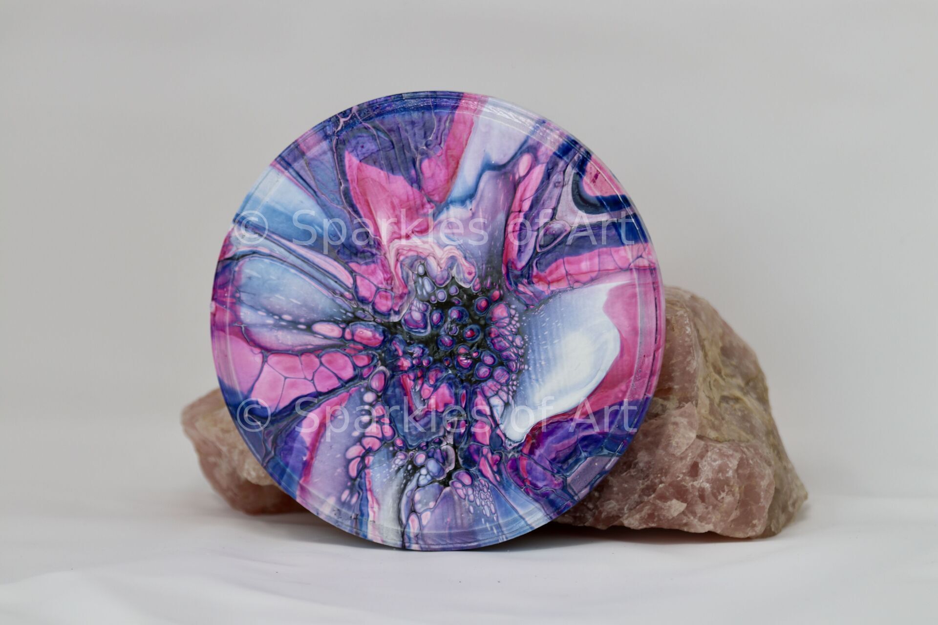 Abstract pink, blue, and purple circular artwork resting on a beige rock