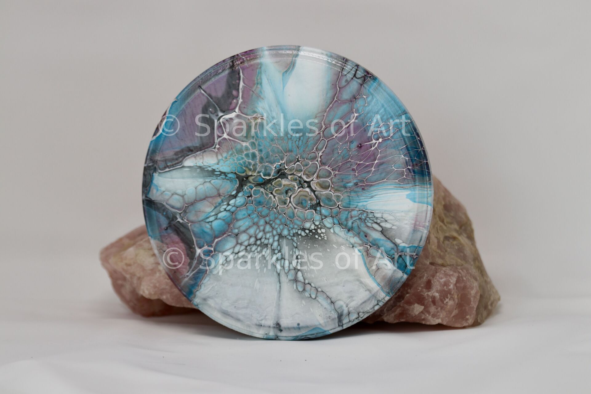 Round blue crystal disc on pink stone base against a gray background