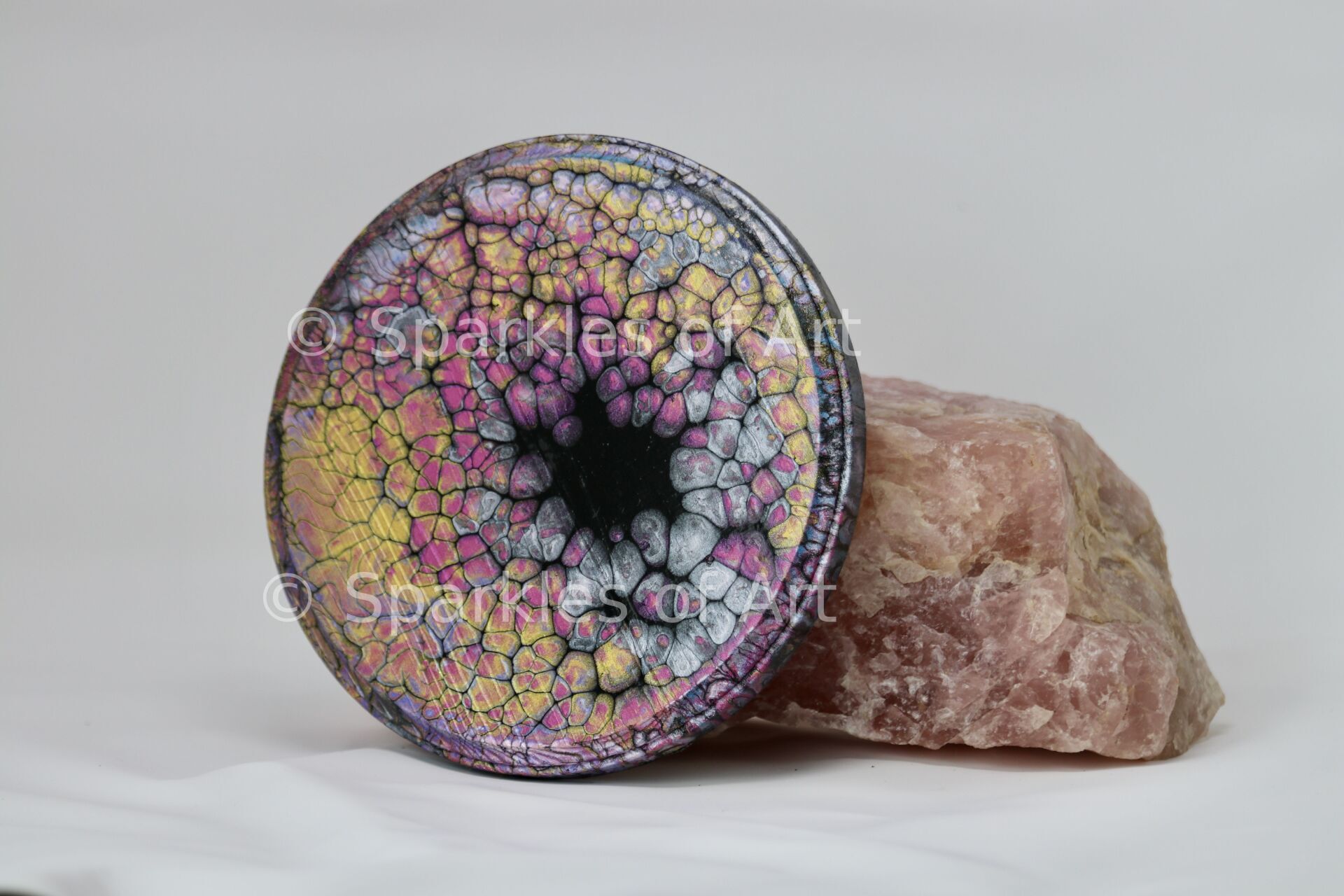 Colorful mosaic candle holder leaning against a rough pink stone on a white background