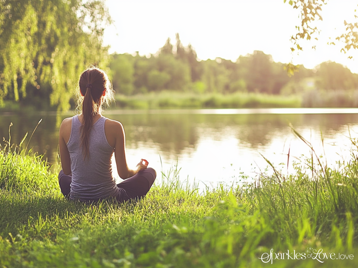 Person meditating on grass by a sunlit lake at sunset