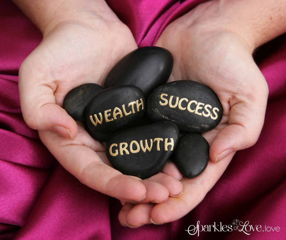 Hands holding black stones labeled “WEALTH,” “SUCCESS,” and “GROWTH” on pink fabric.