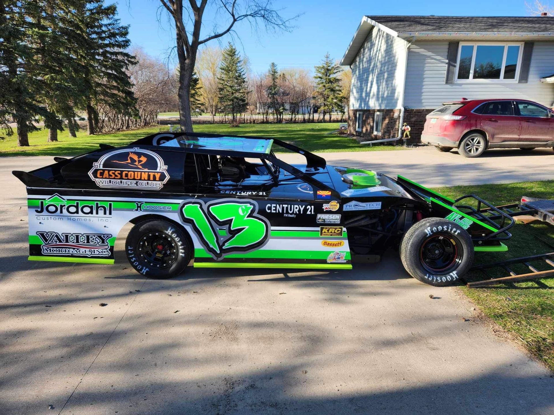 Black and green No. 13 race car parked on a suburban street in front of a house