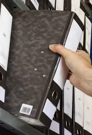 Hand removing a black file folder from a shelf with other files.