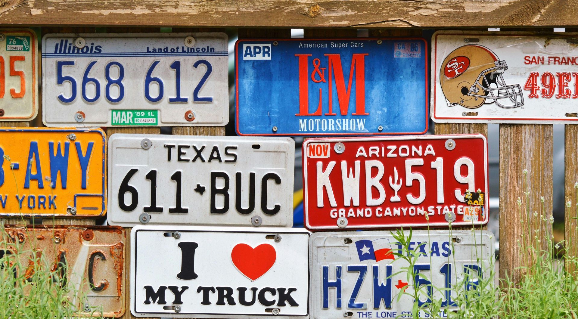 Collection of colorful license plates mounted on a wooden fence.