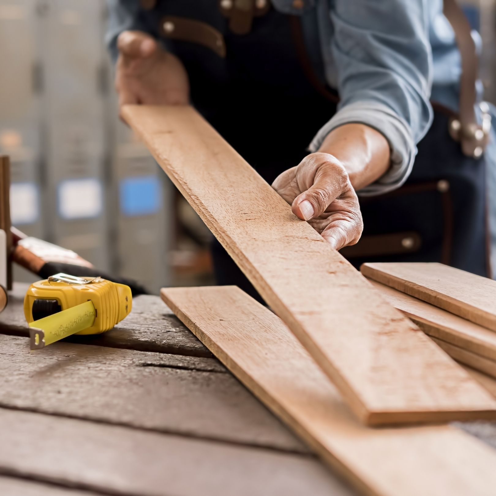 Hands measuring wooden planks on a workbench with a yellow tape measure nearby.