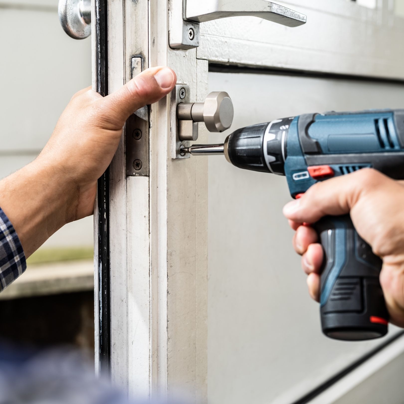 Hands using a drill to install hardware on a white garage door frame