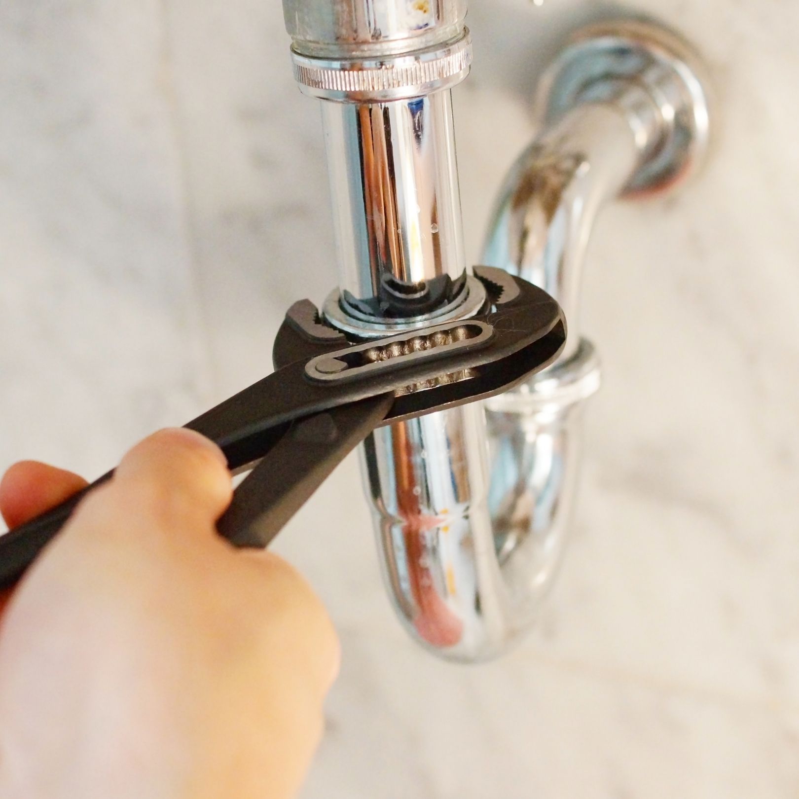 Hand turning a wrench to tighten a chrome pipe fitting under a sink