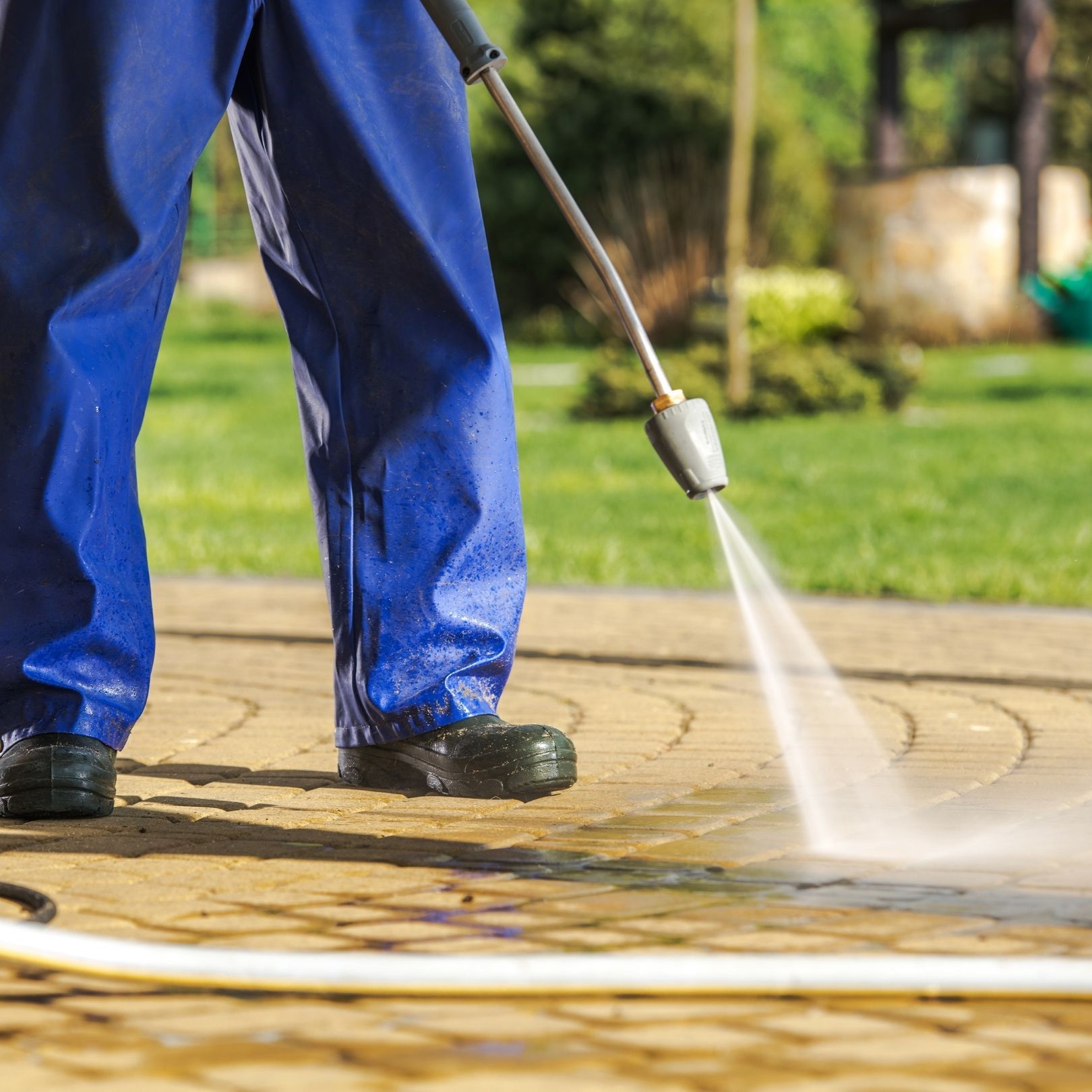 Person pressure-washing a wet patio, with blue pants and black boots.
