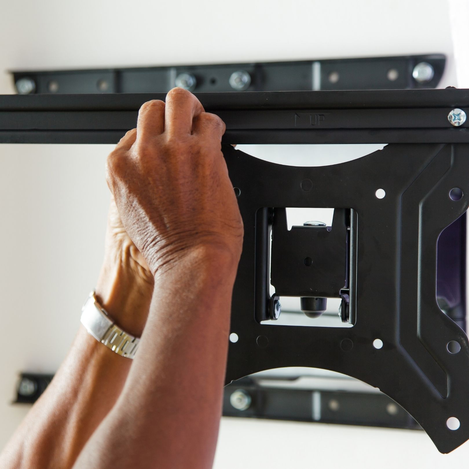 Hands installing a black wall-mount bracket with a level attached.