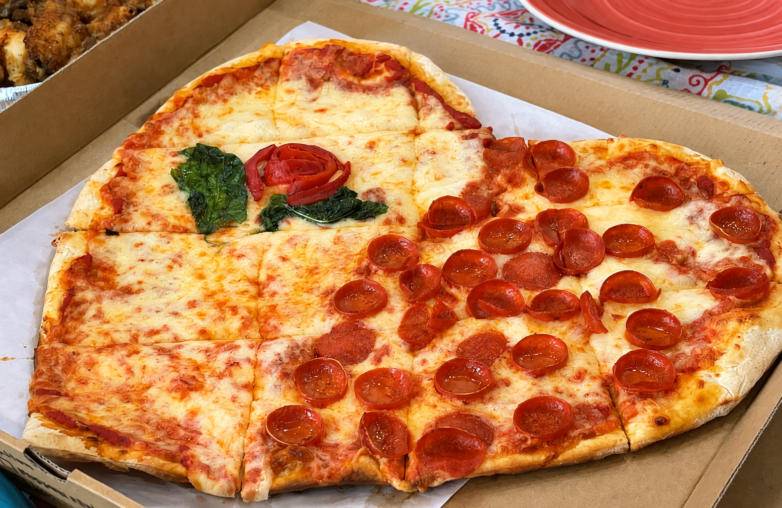 Heart-shaped pepperoni and cheese pizza in a box, topped with a basil leaf and tomato rose.