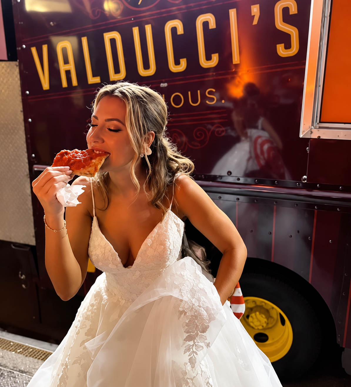 Woman in a white dress eating pizza beside a Valducci’s food truck