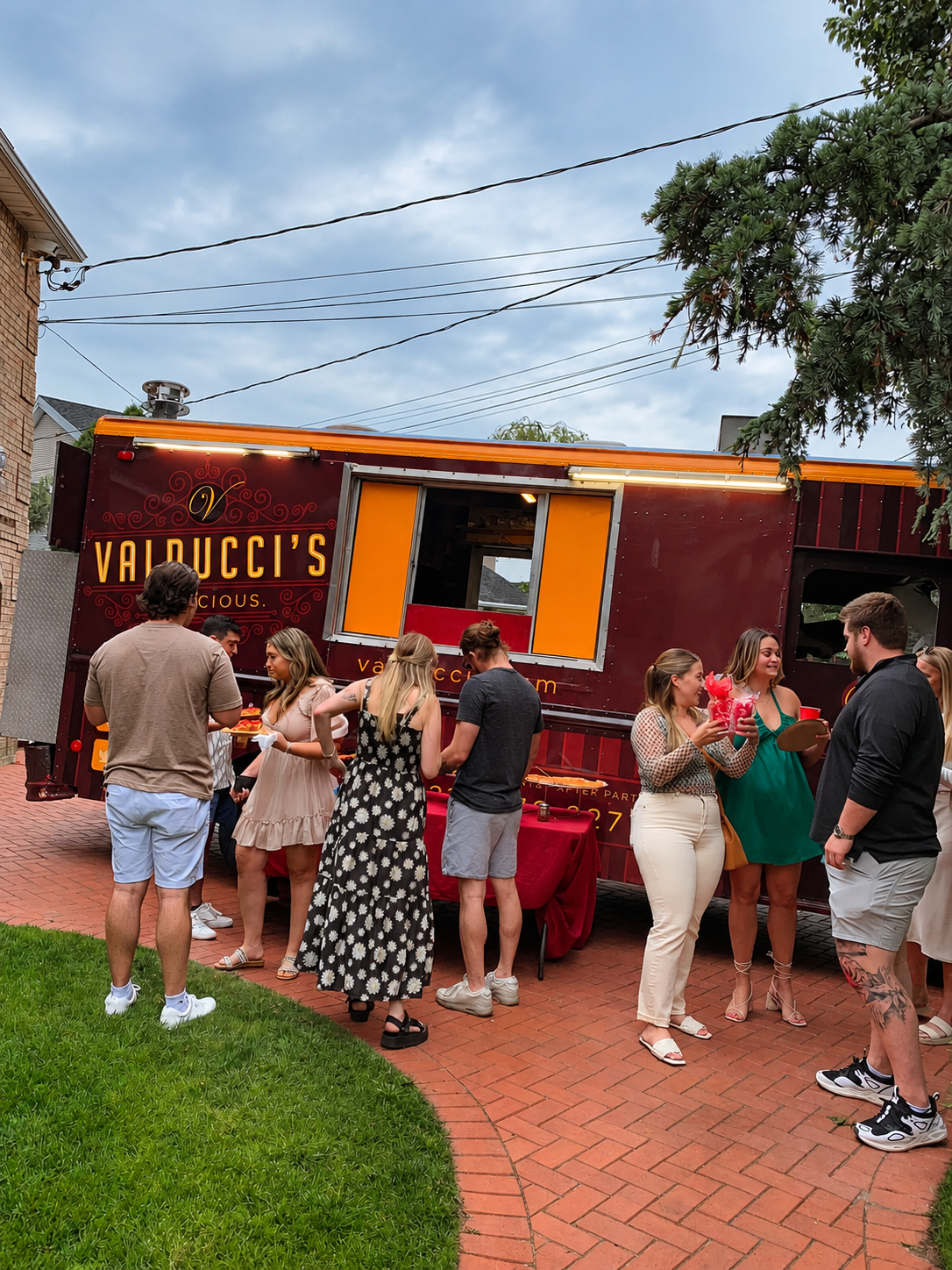People standing outside Yaluzzi’s food truck on a brick patio, with orange and red walls.