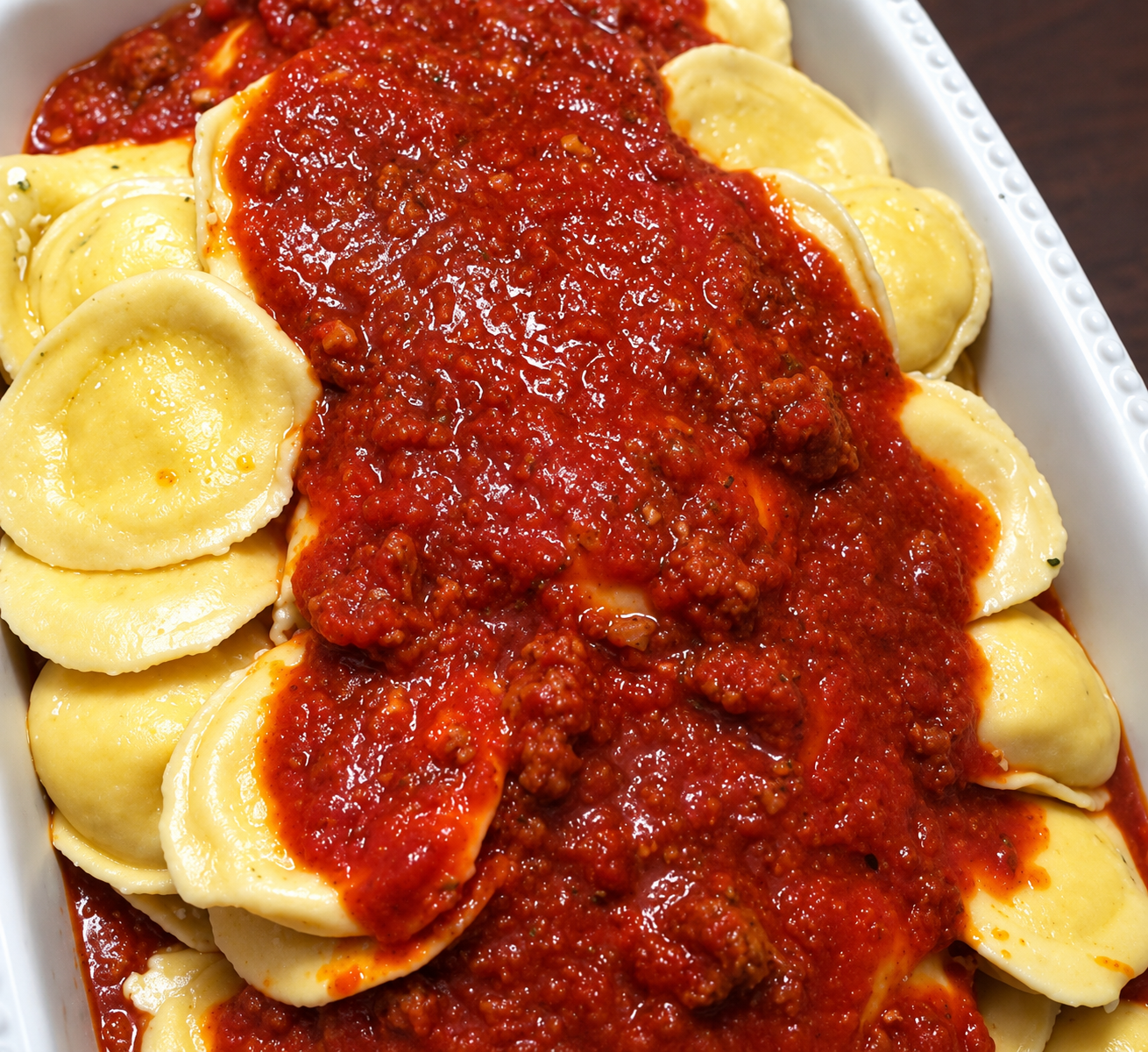 Ravioli covered in red tomato sauce in a white takeout container