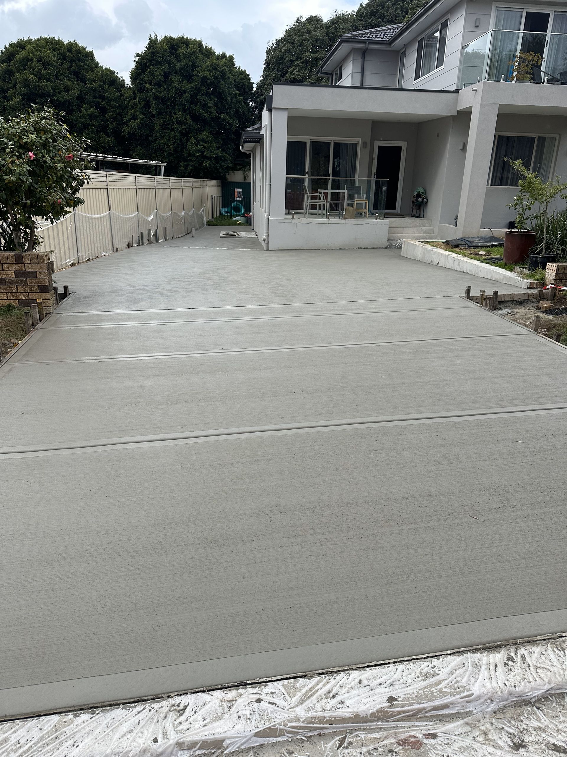 Newly poured concrete driveway extending to a light-colored house with a small porch; overcast sky.