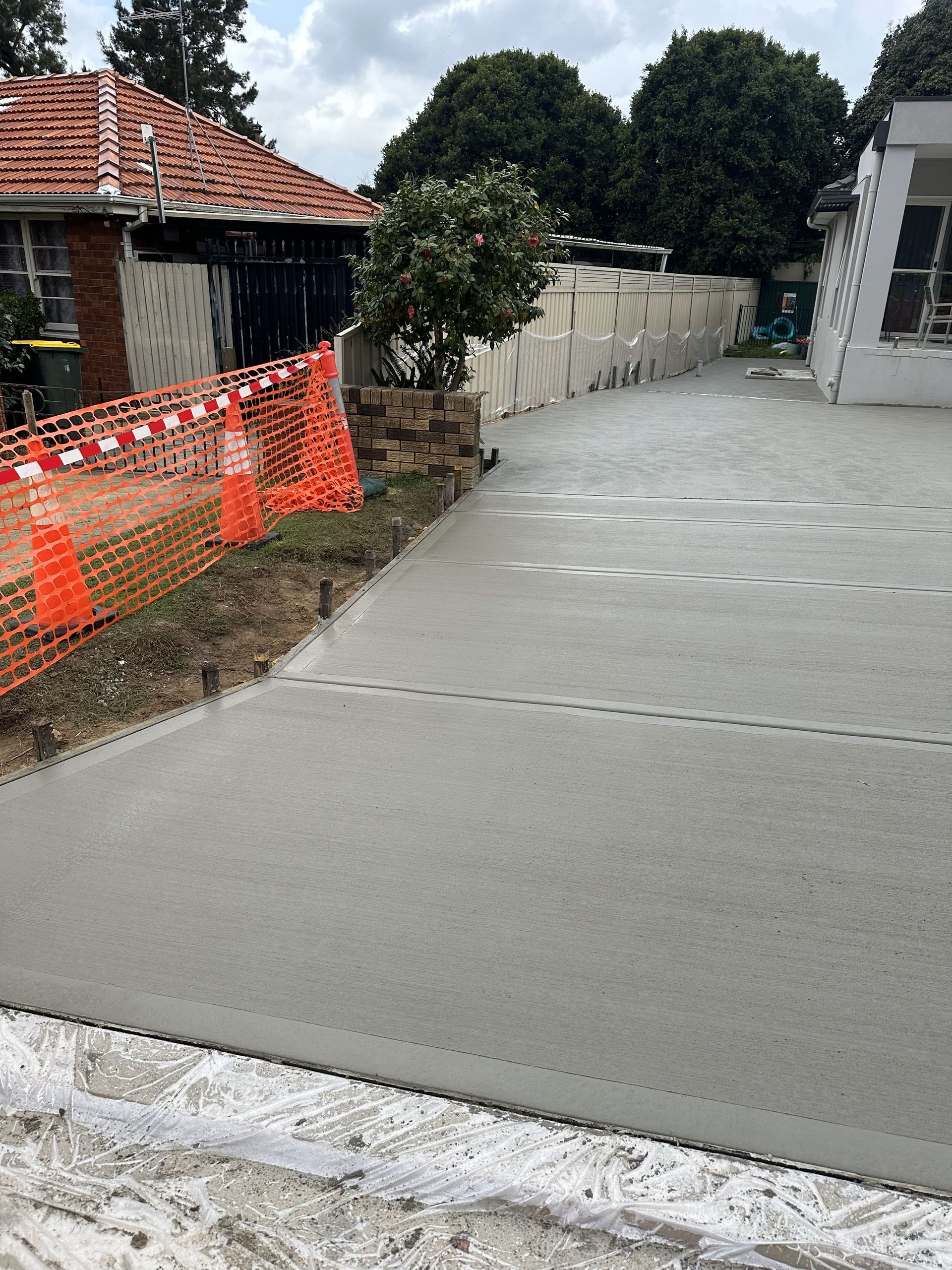 Newly poured concrete driveway with orange safety fence and cones along the edge of the grass.