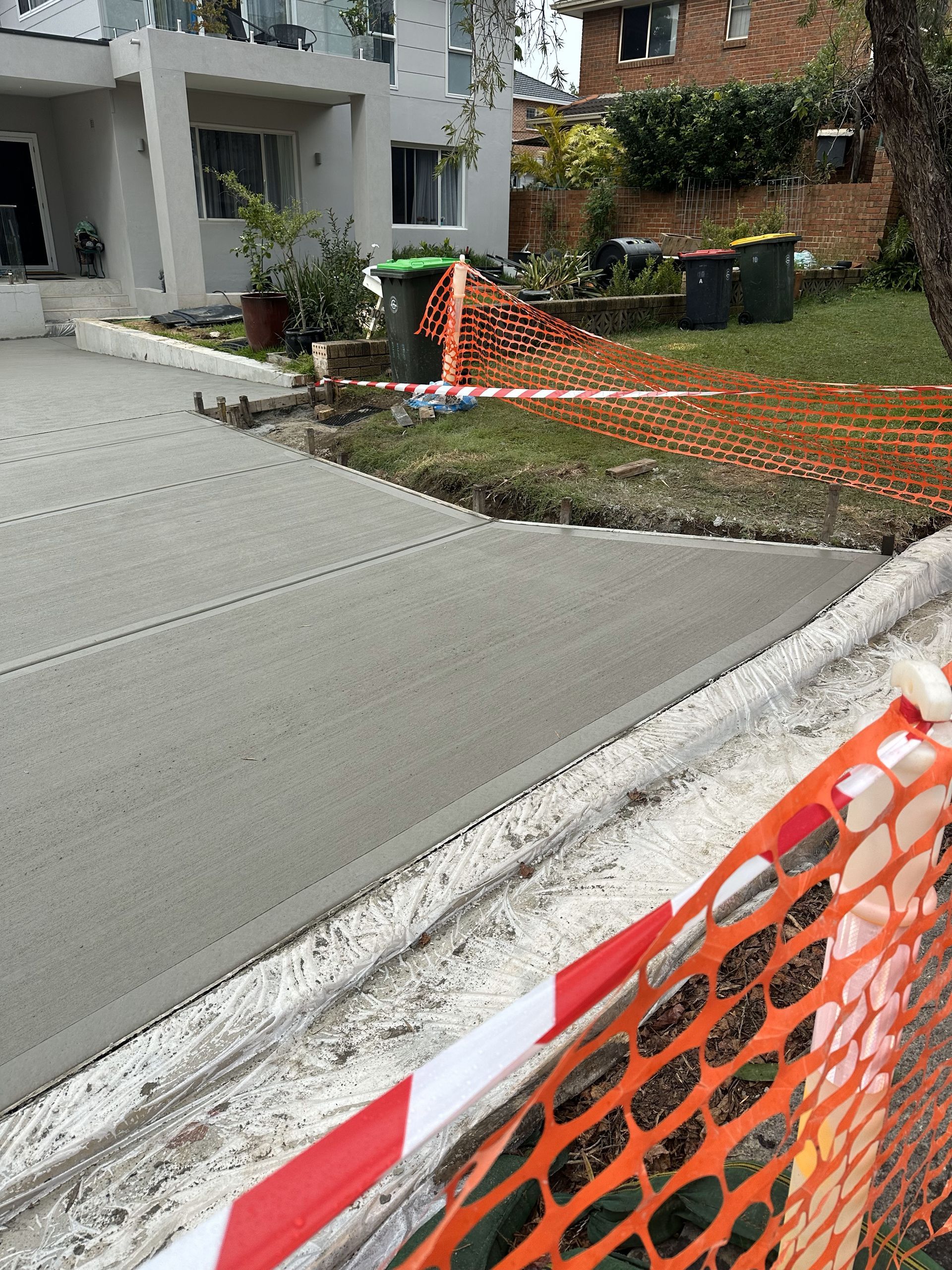Freshly poured concrete driveway with safety fencing, in front of a light-colored building.