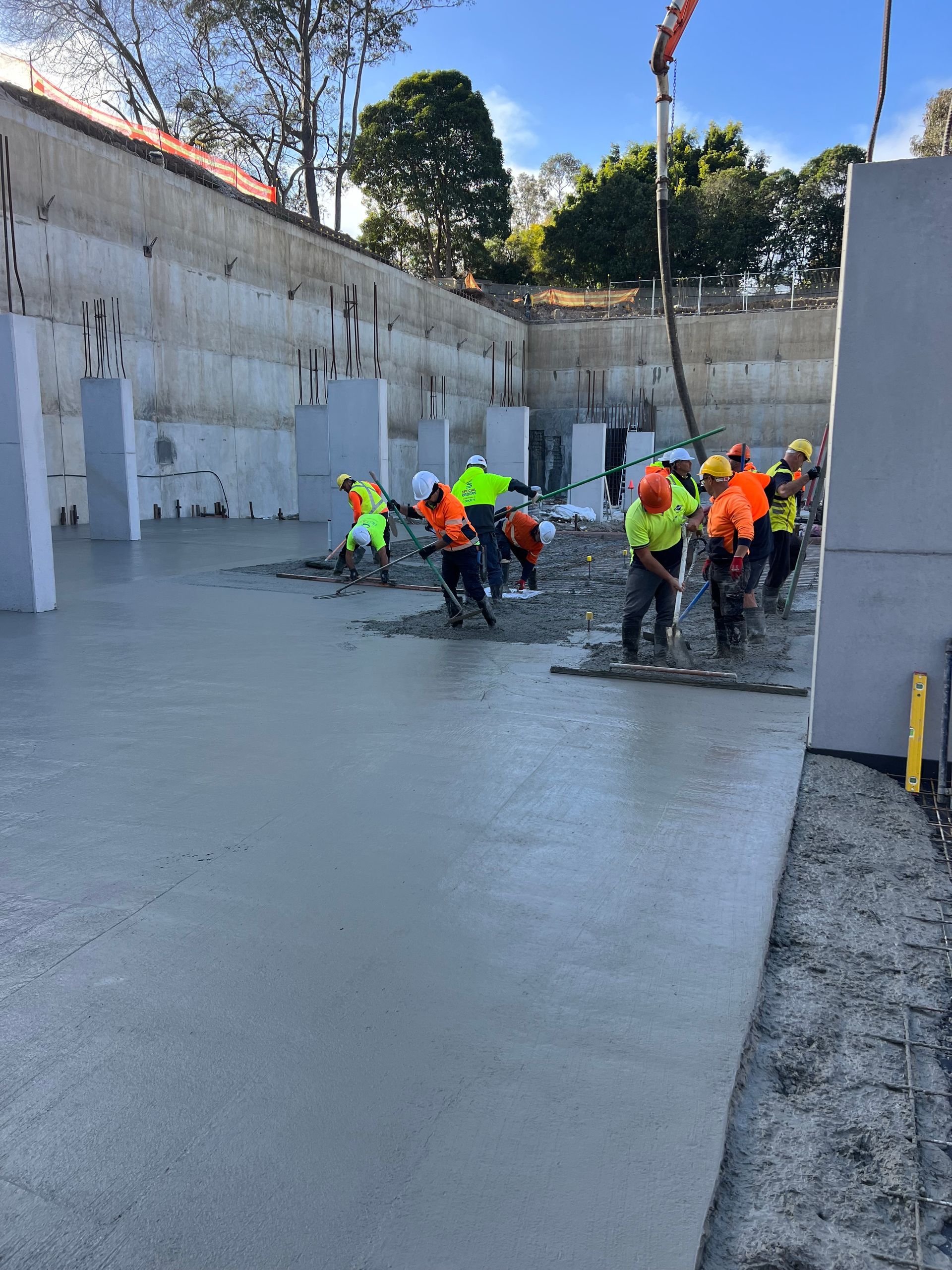 Construction workers pouring and smoothing concrete at a building site. Workers wear hard hats and safety vests.