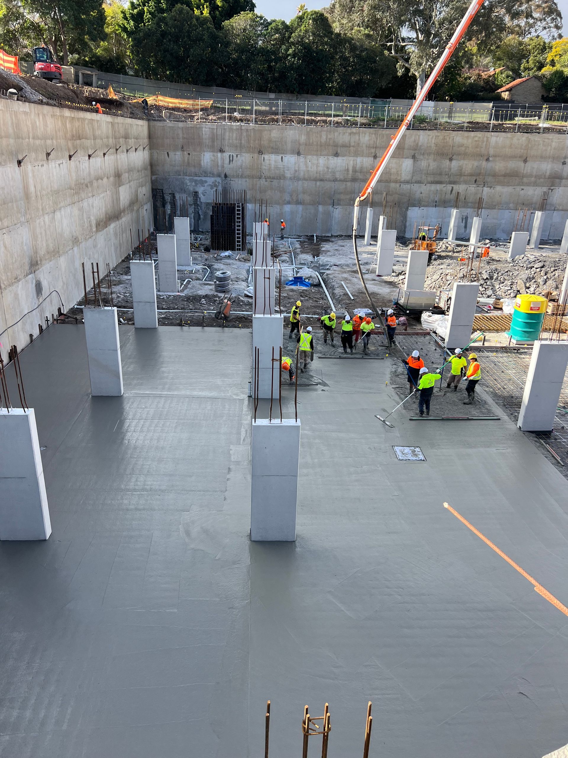 Construction site with workers pouring concrete floor around pillars.