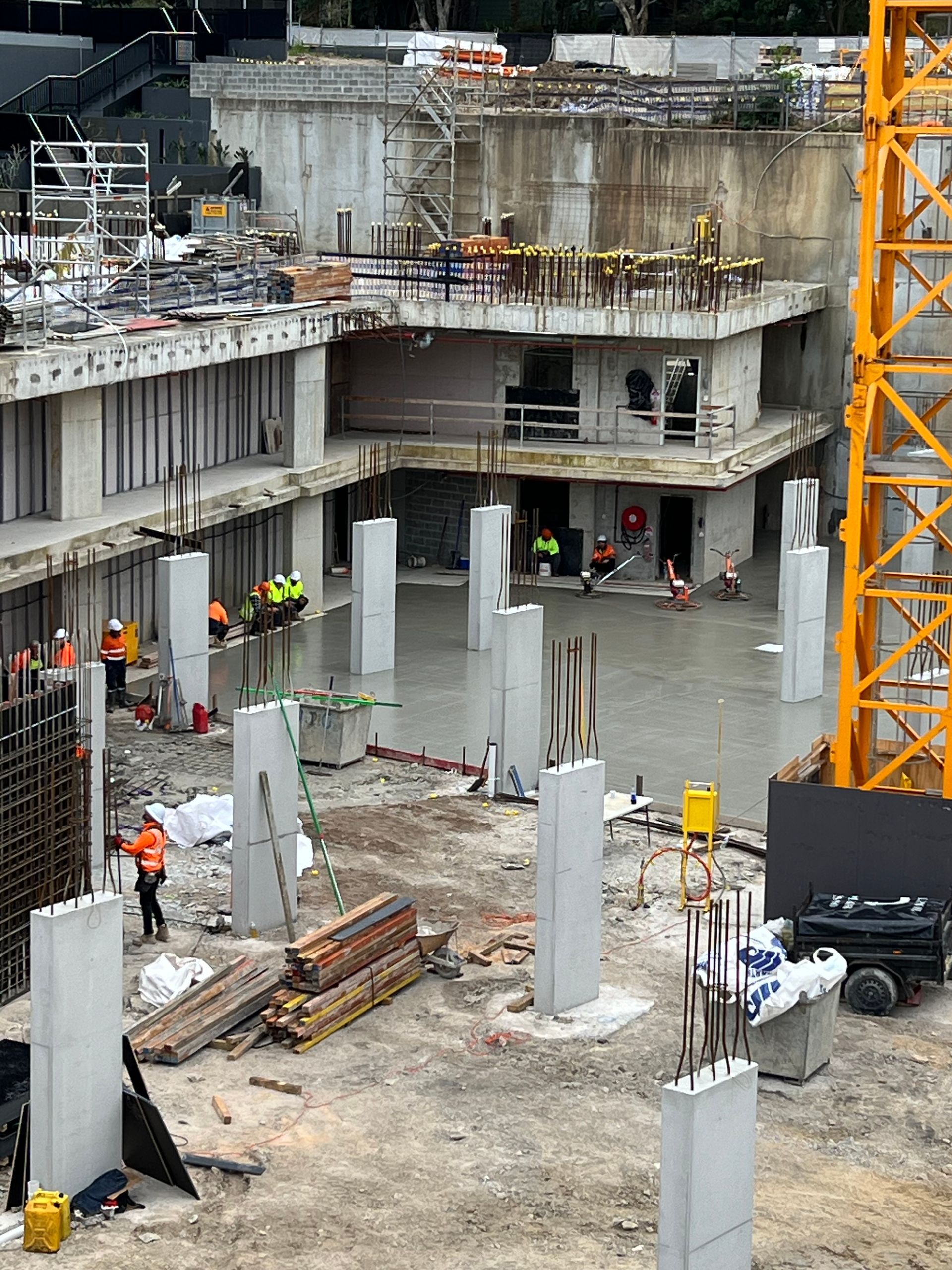 Construction site with workers, concrete structures, and yellow crane.