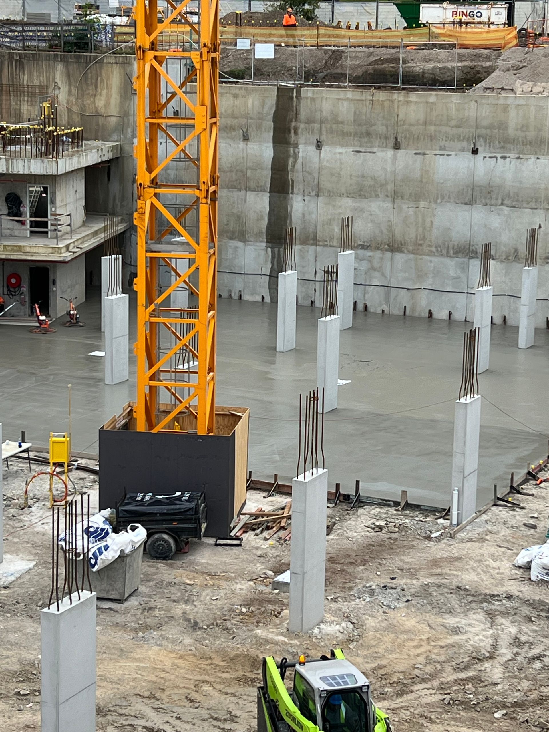 Construction site with a yellow crane and concrete pillars in a large pit.