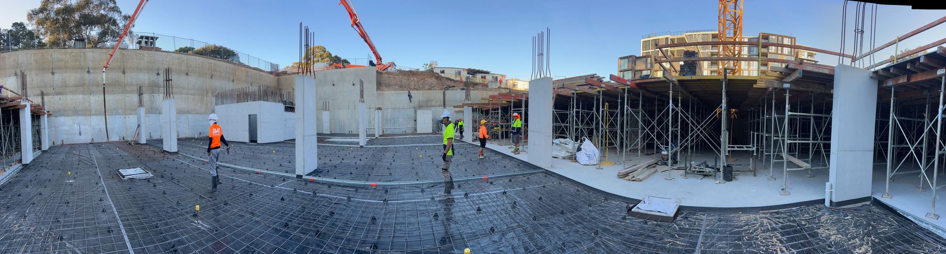 Construction site with concrete forms, workers in safety vests, and a clear blue sky.