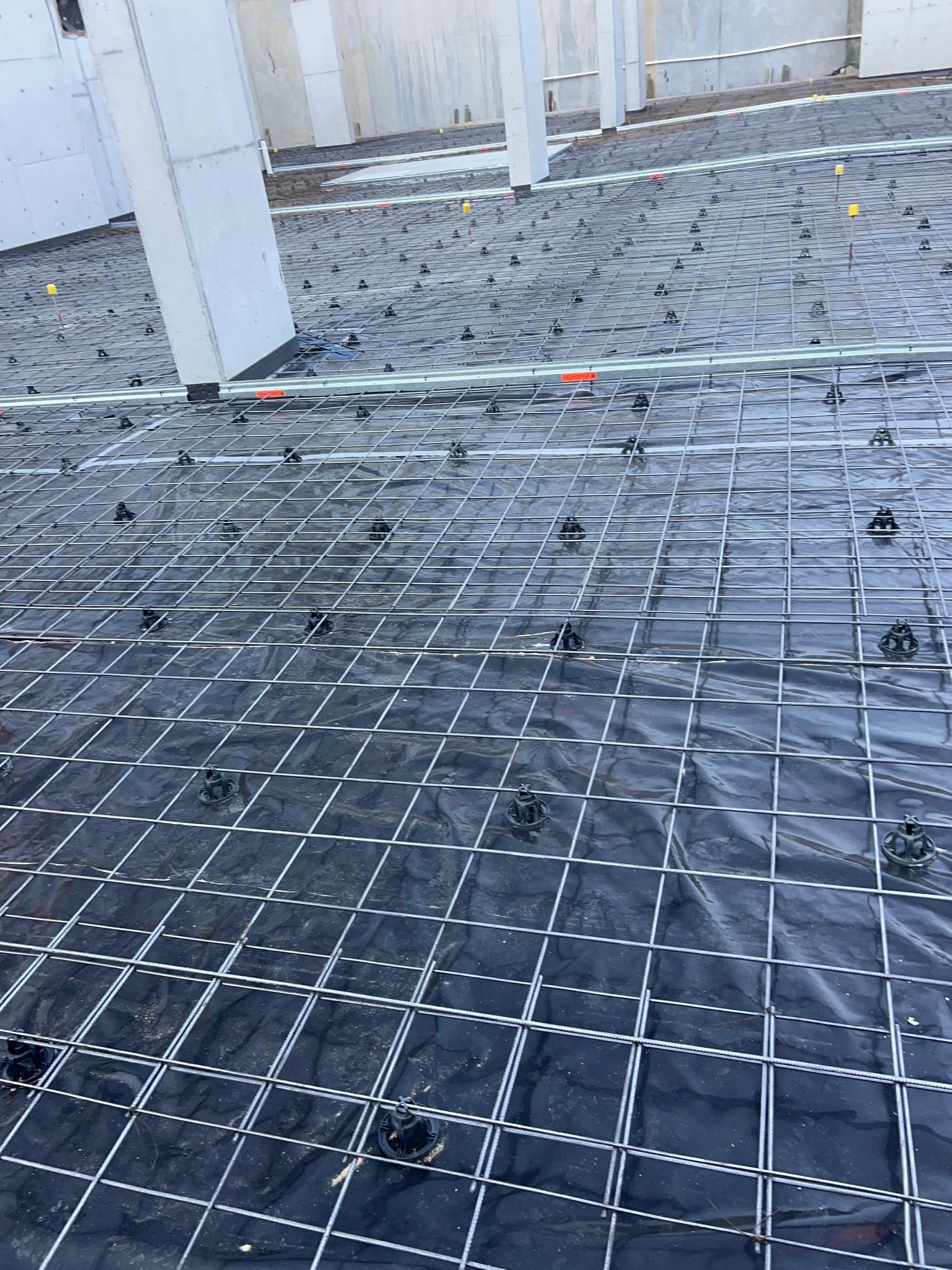 Construction site with rebar grid and black plastic sheeting, ready for concrete pouring.