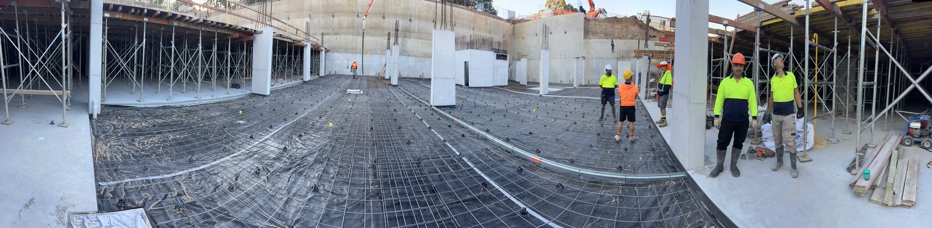 Construction site: Workers in neon vests and helmets near concrete pillars and scaffolding.