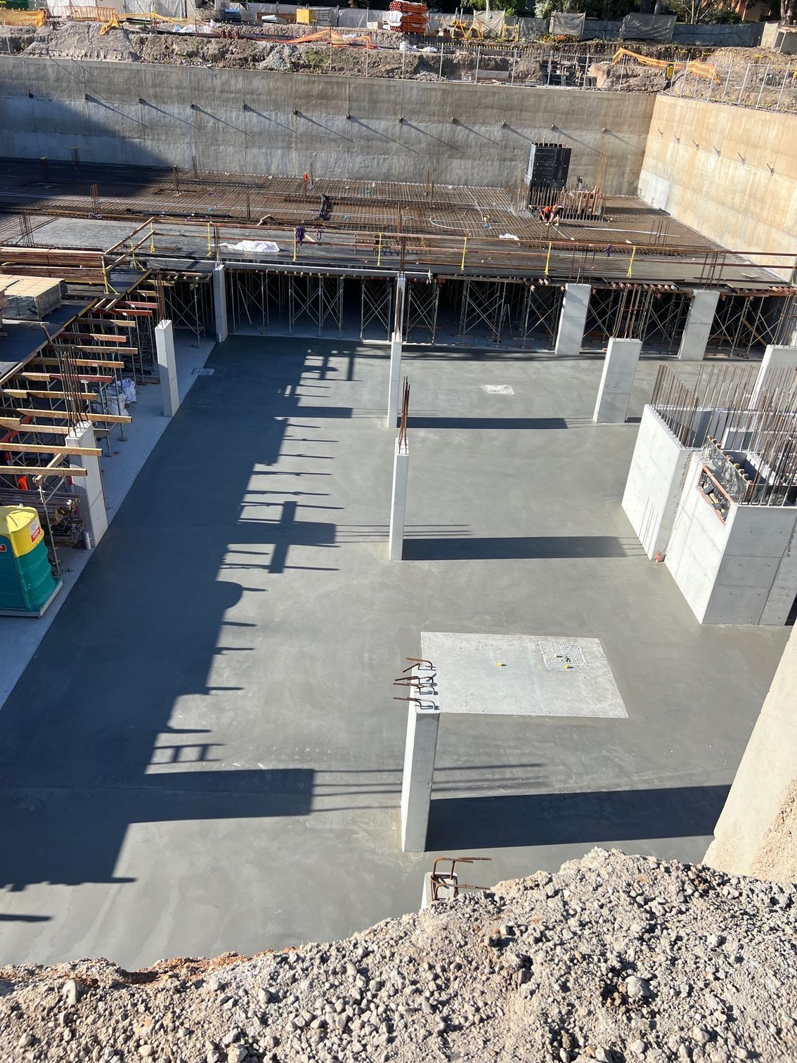 Construction site with concrete foundation and pillars, surrounded by earth walls and building materials.