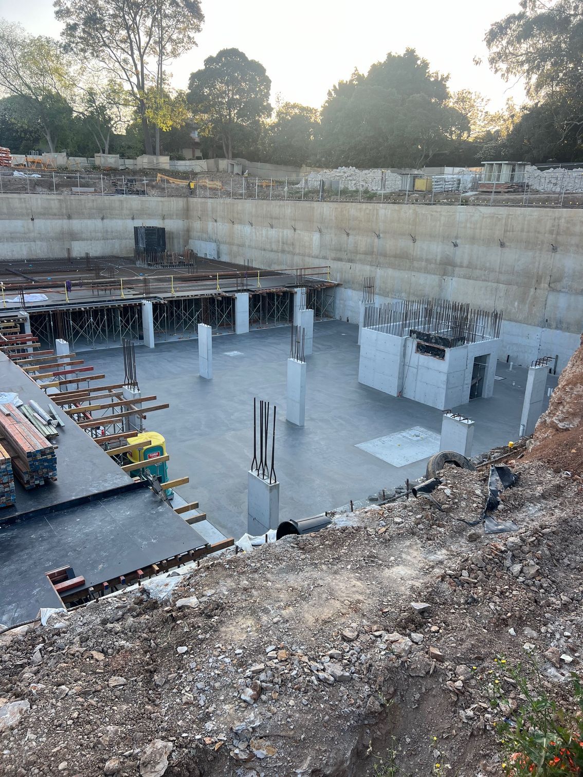 Construction site: large excavated area with concrete foundations, pillars, and retaining walls.