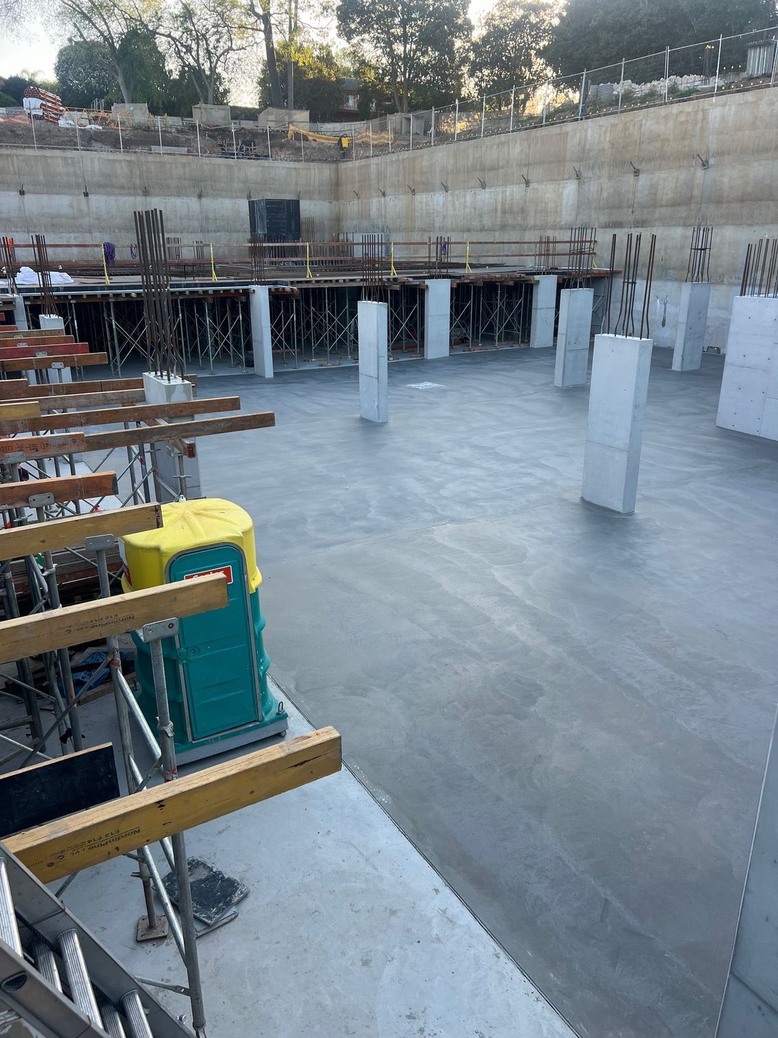 Construction site with concrete floor and pillars; portable toilet and scaffolding visible.