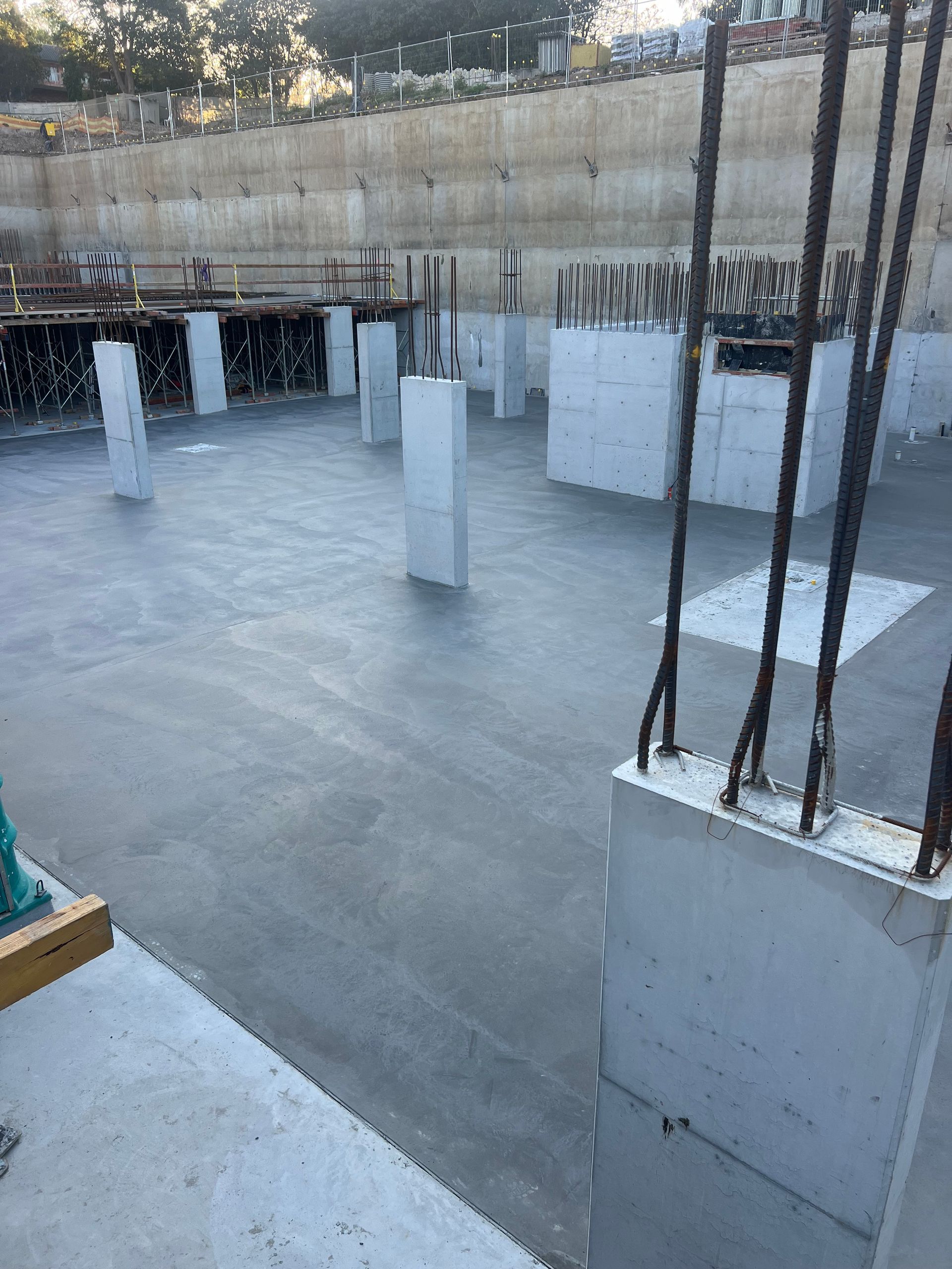 Construction site with concrete pillars and a freshly poured concrete foundation.