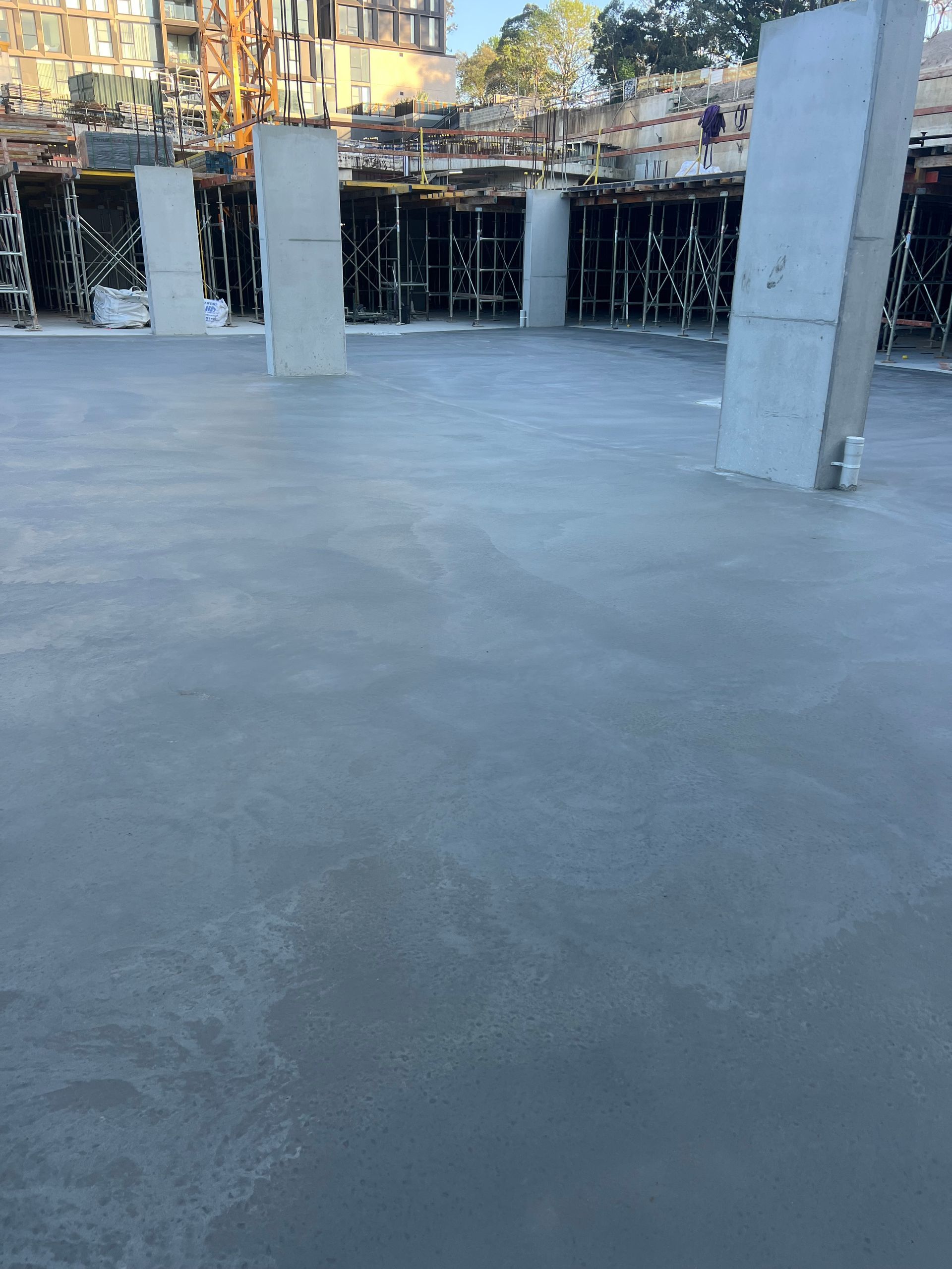 Concrete floor of a building under construction, with support columns and scaffolding visible.