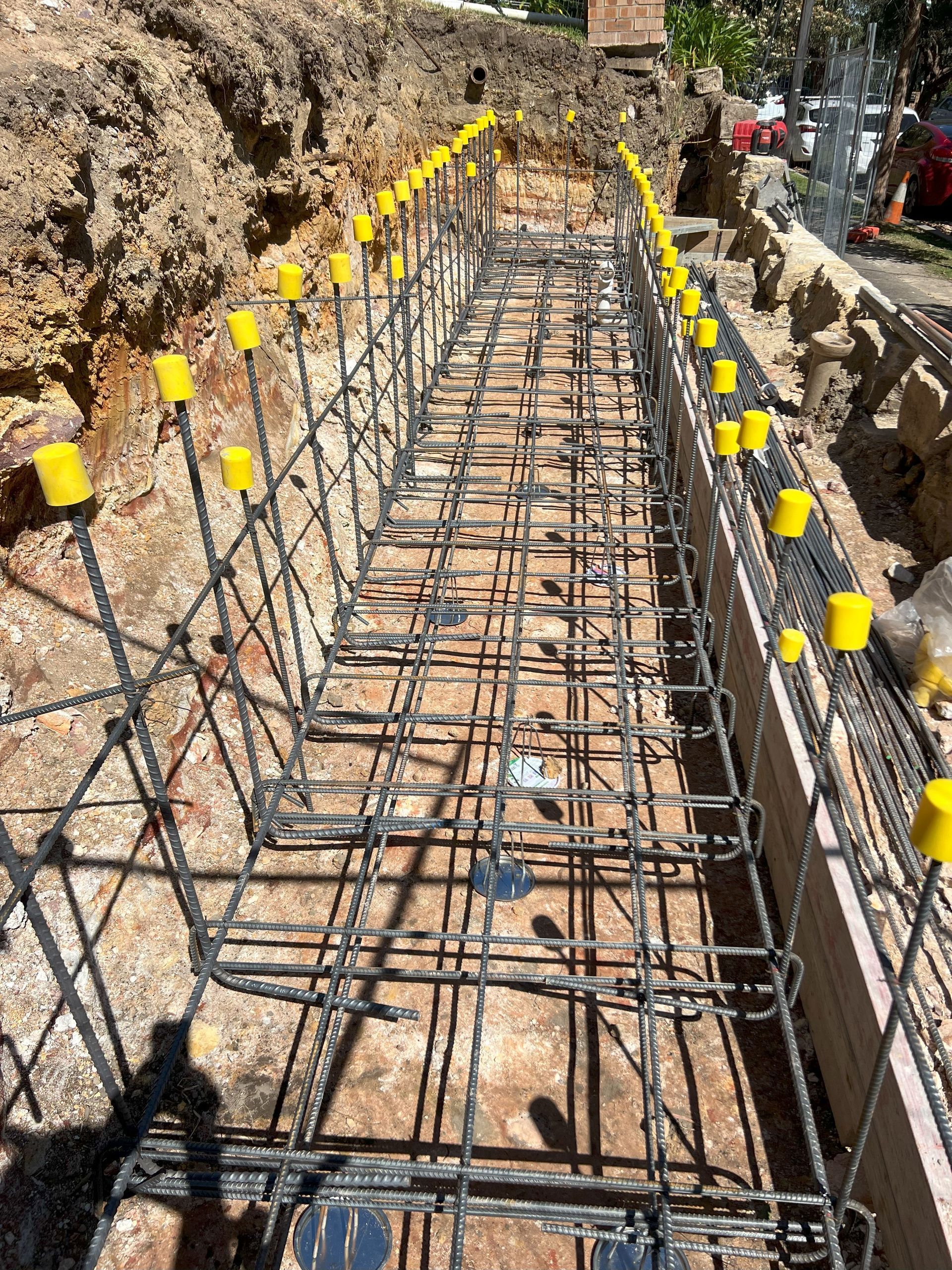 Reinforcement bars arranged for concrete foundation, yellow protective caps visible.