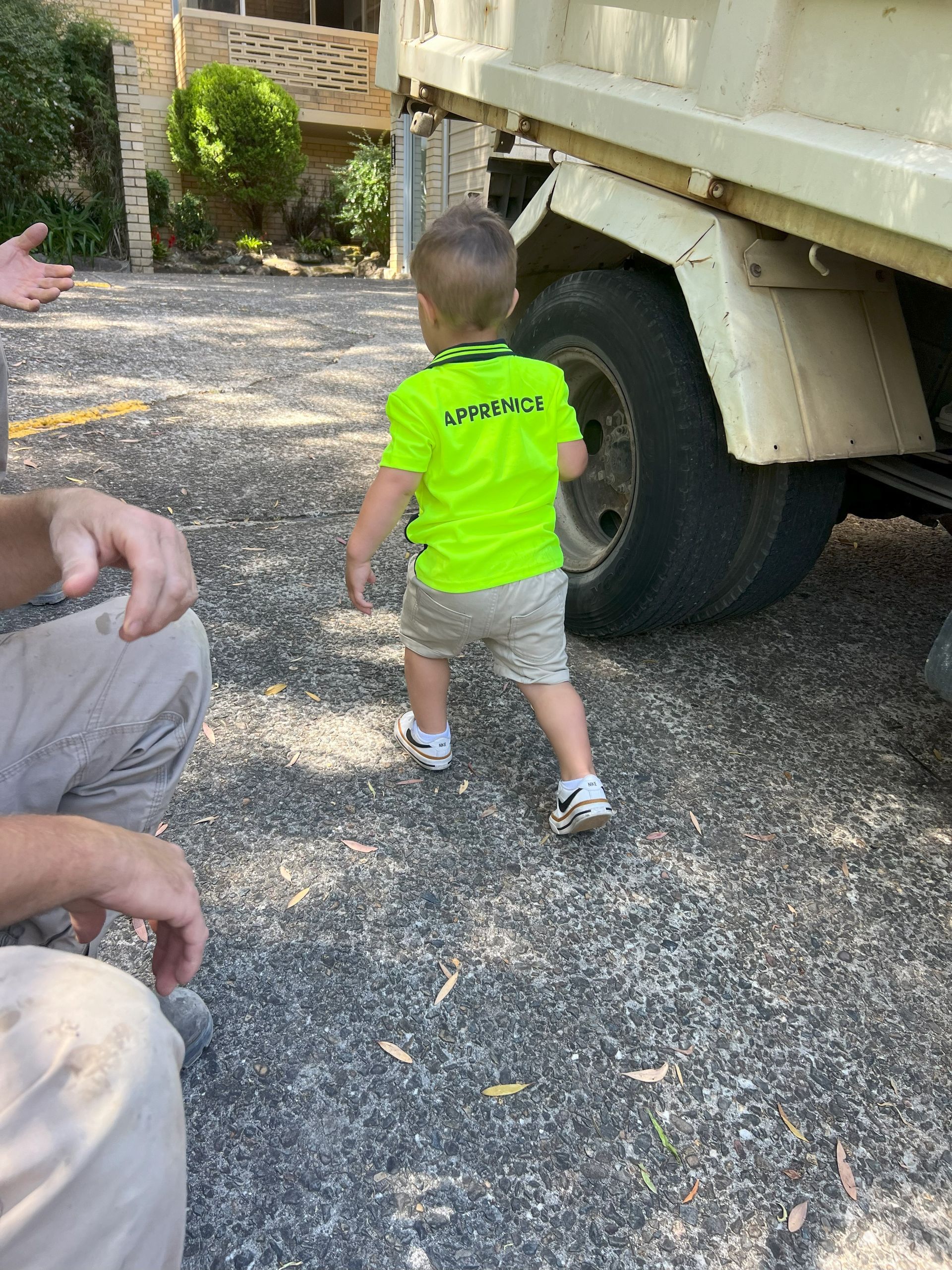 Child in neon green shirt walking toward large truck tire on a gravel road.