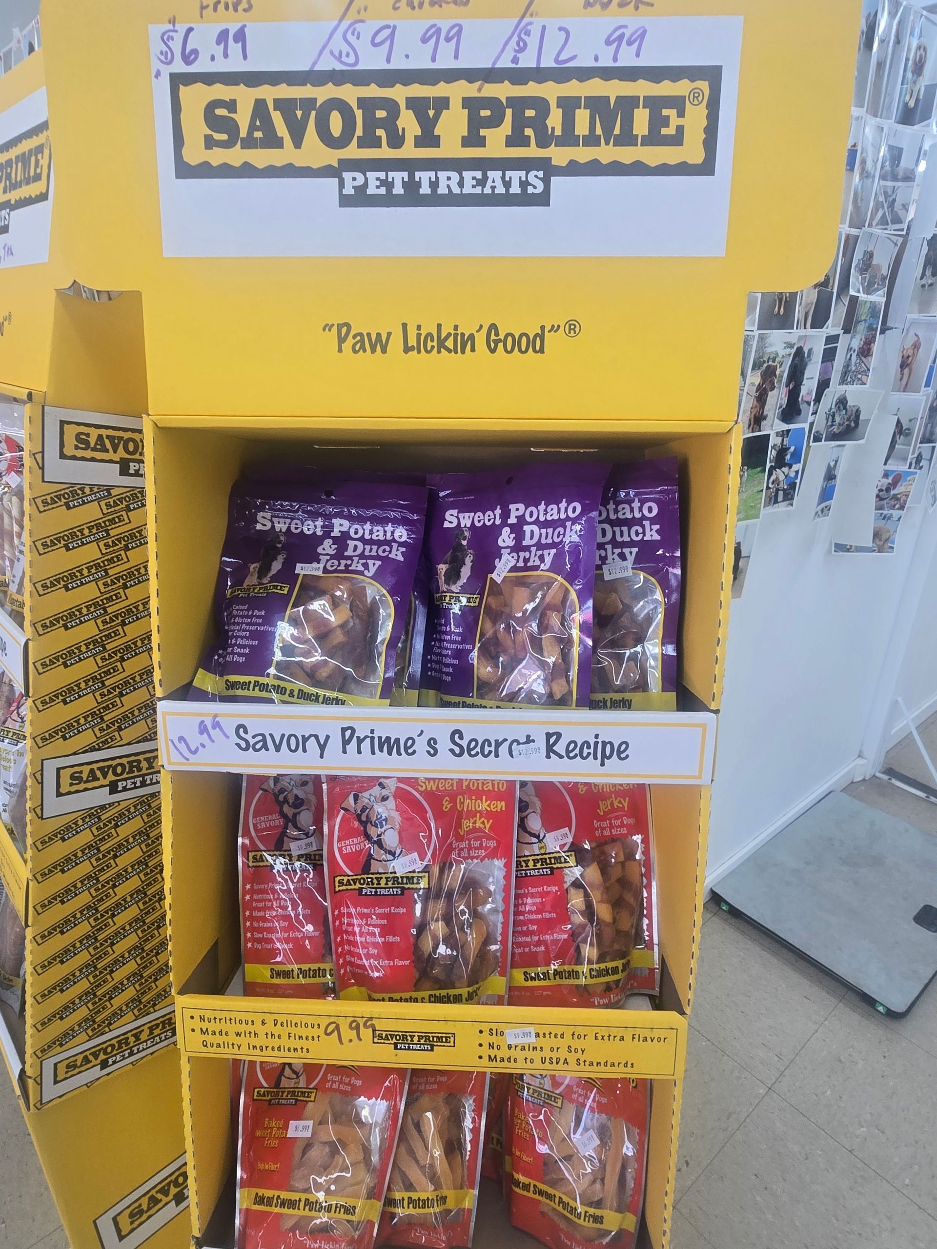 A yellow retail display stand featuring Savory Prime pet treats with handwritten pricing on the top shelf.