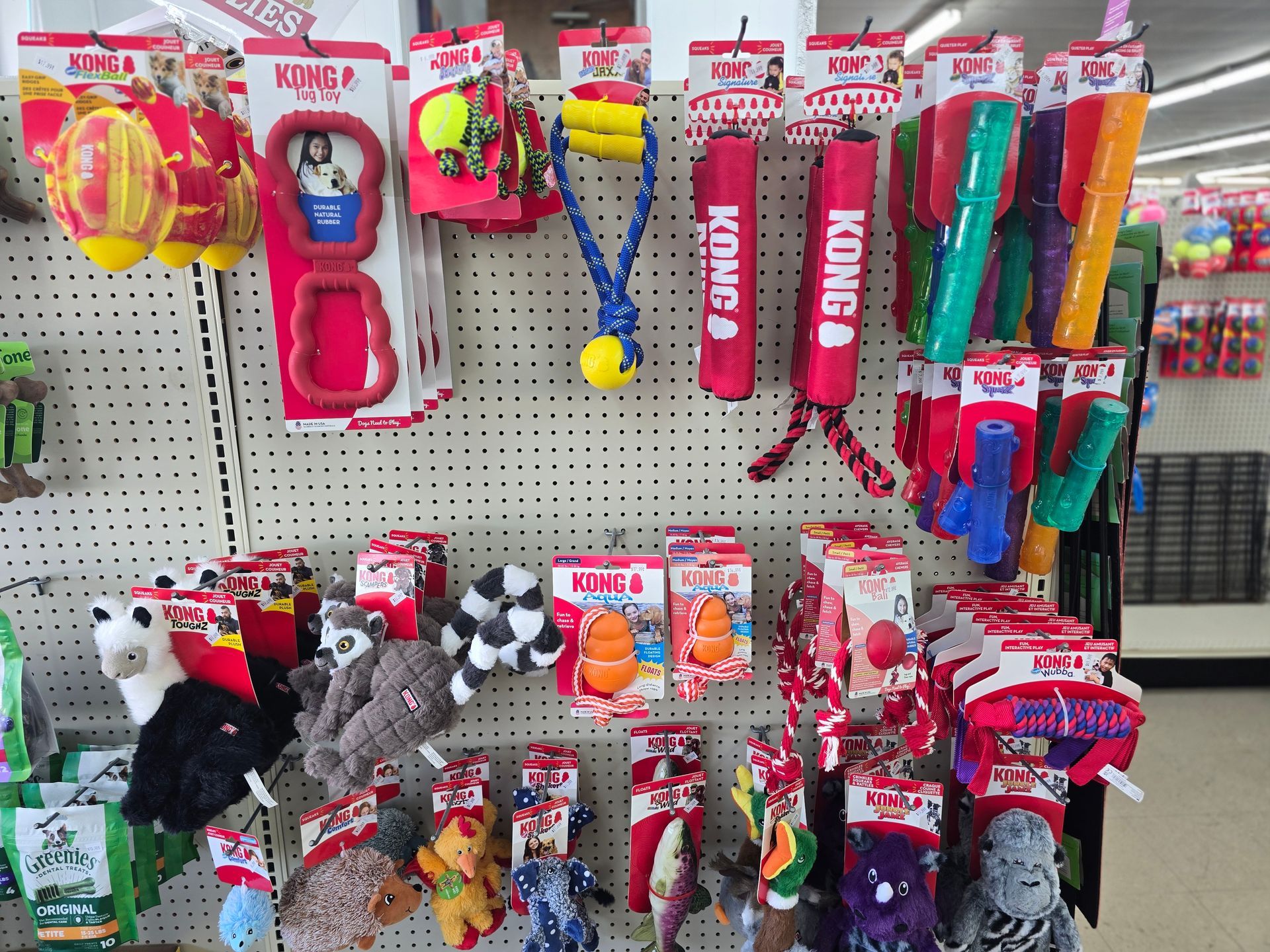 A retail store shelf displays various KONG brand dog toys, including rubber chew toys, rope toys, and plush stuffed animals.