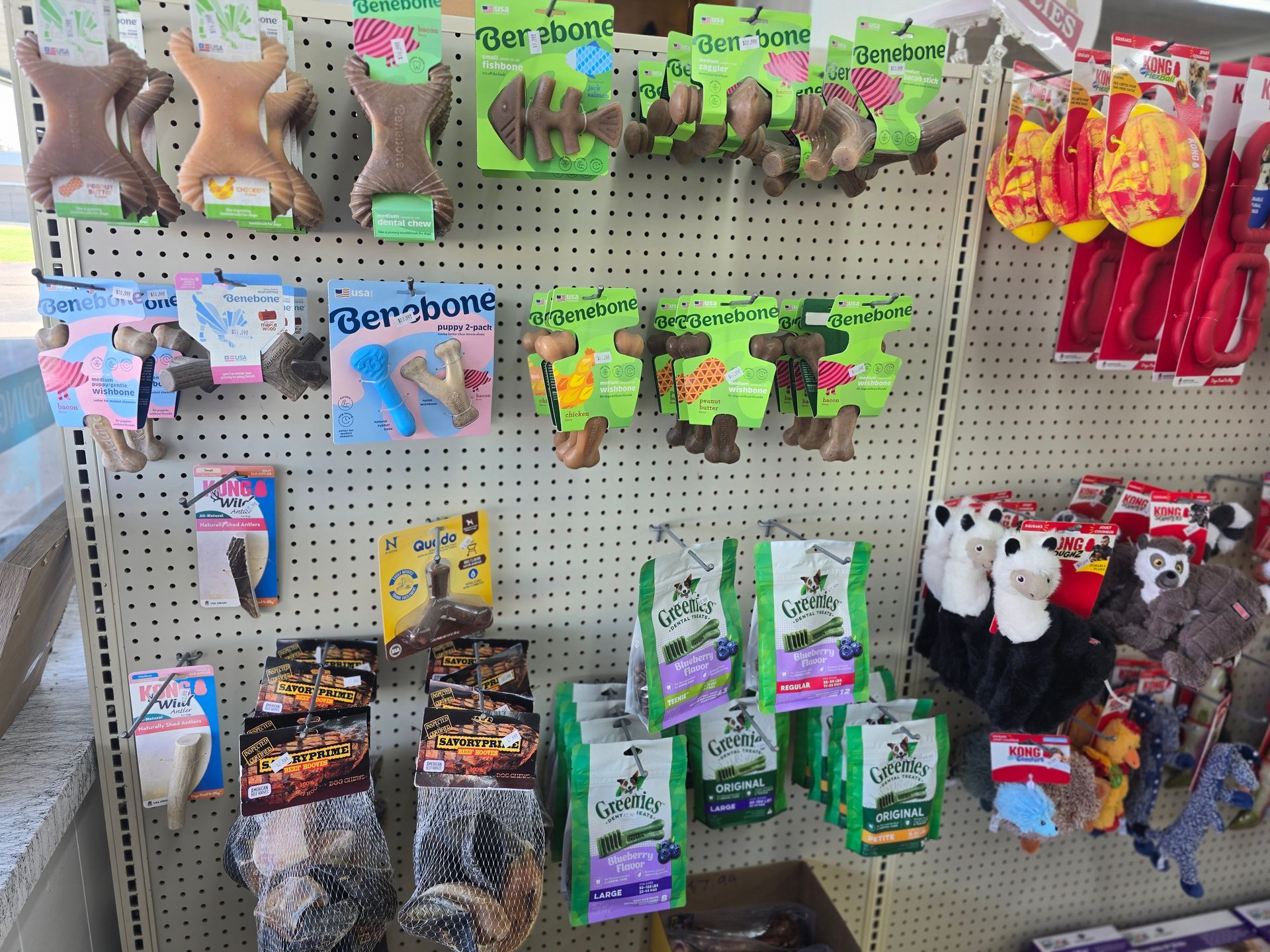 Retail store shelf display featuring various dog toys, including chew bones, bone-shaped treats, and stuffed animals.