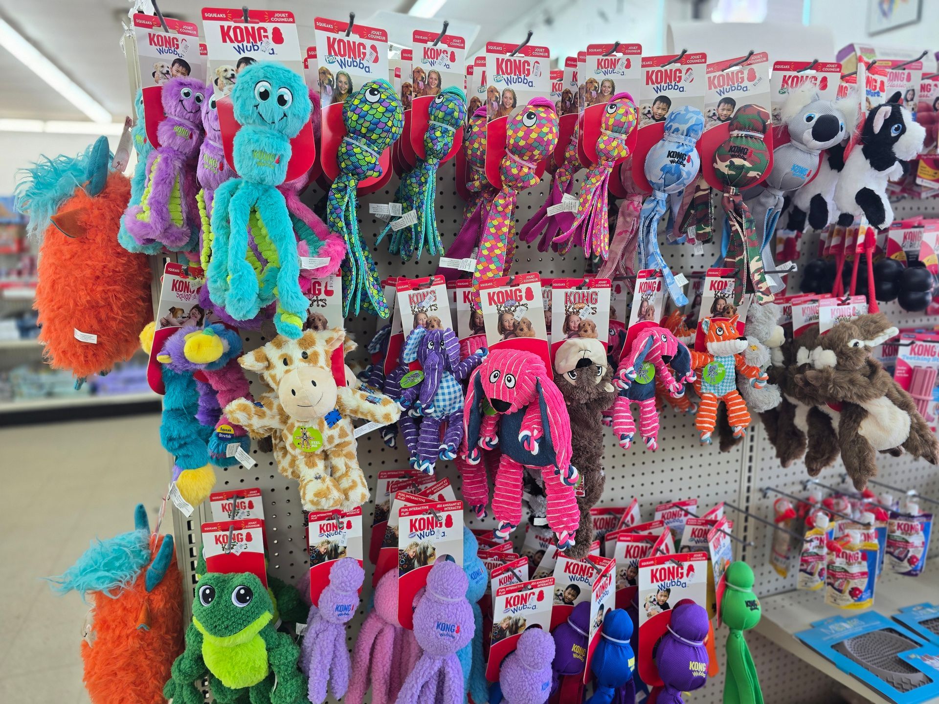 A retail store shelf display filled with various colorful, plush animal dog toys hanging from hooks.