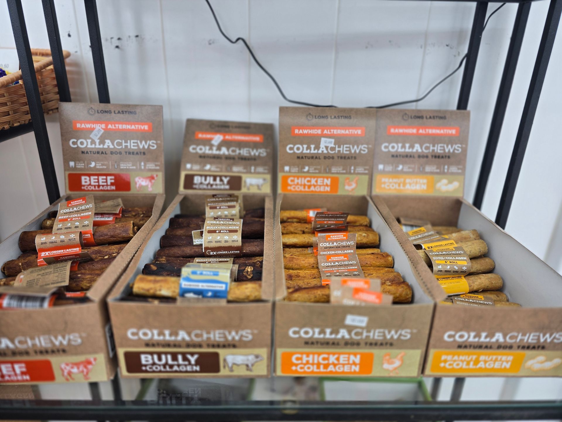Four boxes of CollaChews dog treats on a store shelf, labeled Beef, Bully, Chicken, and Peanut Butter, all with collagen.