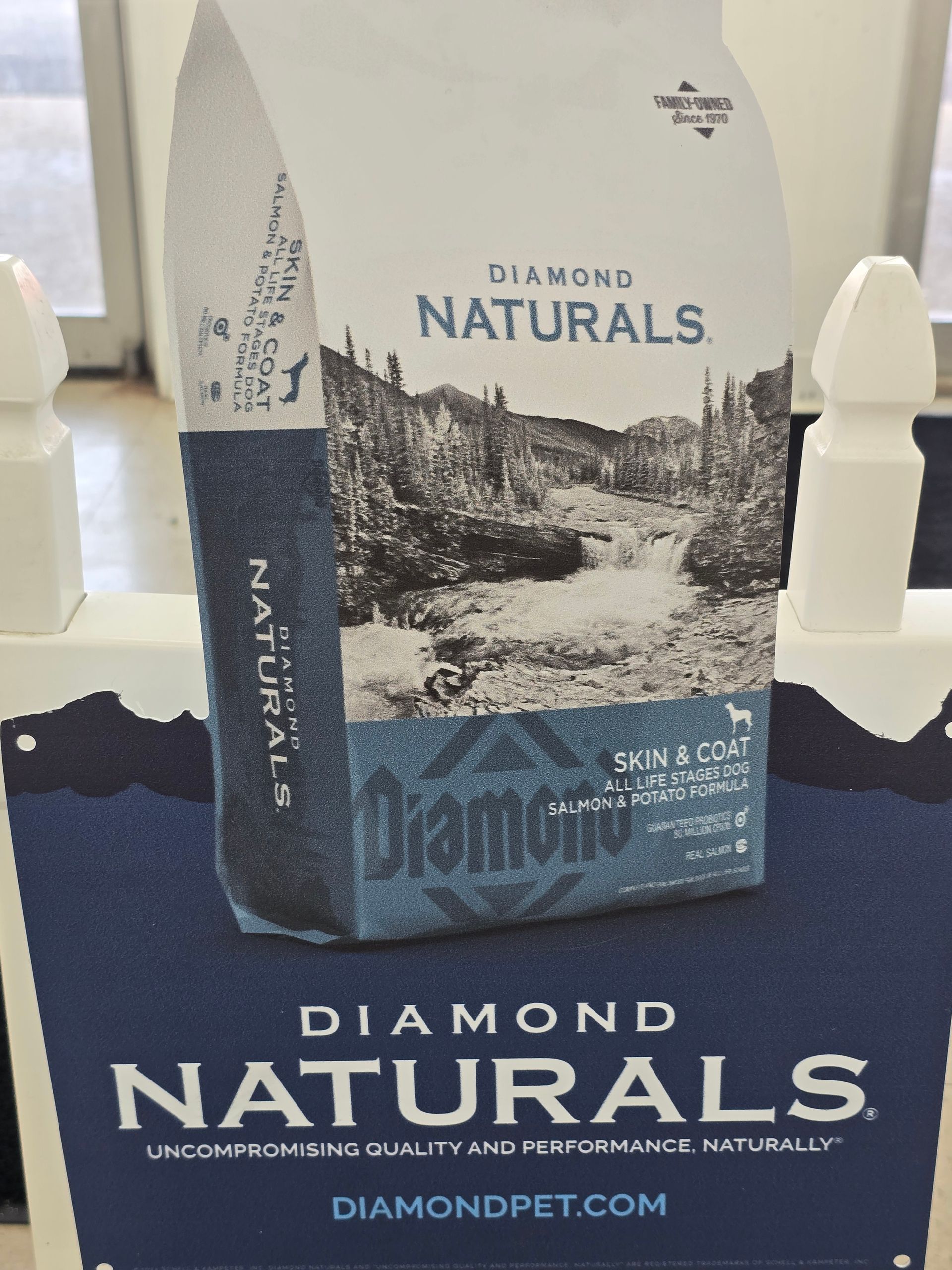 A bag of Diamond Naturals dog food sitting on a white display stand with brand branding below.
