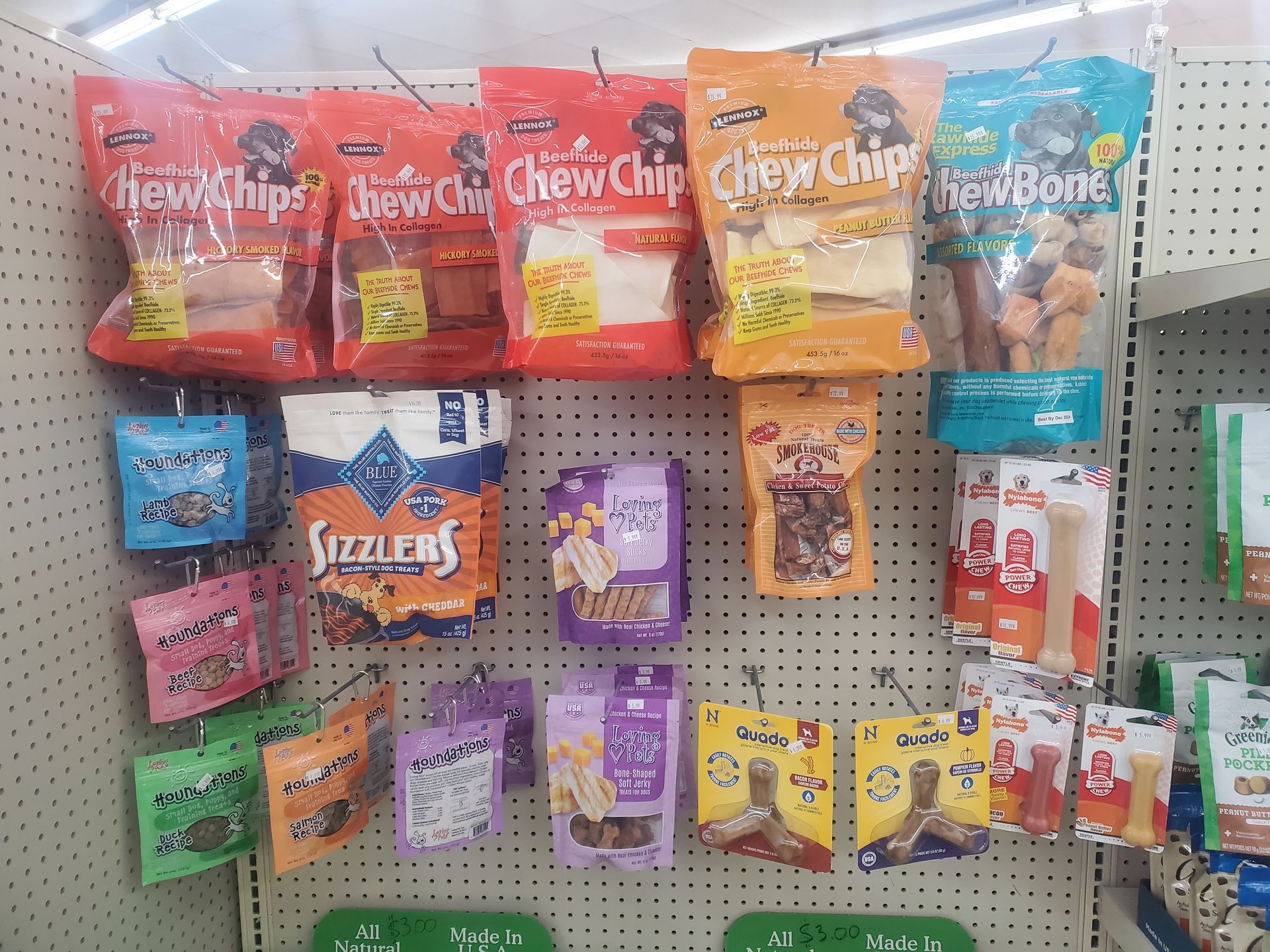 A pegboard display in a store featuring various brands and colorful packages of dog treats and chew toys.