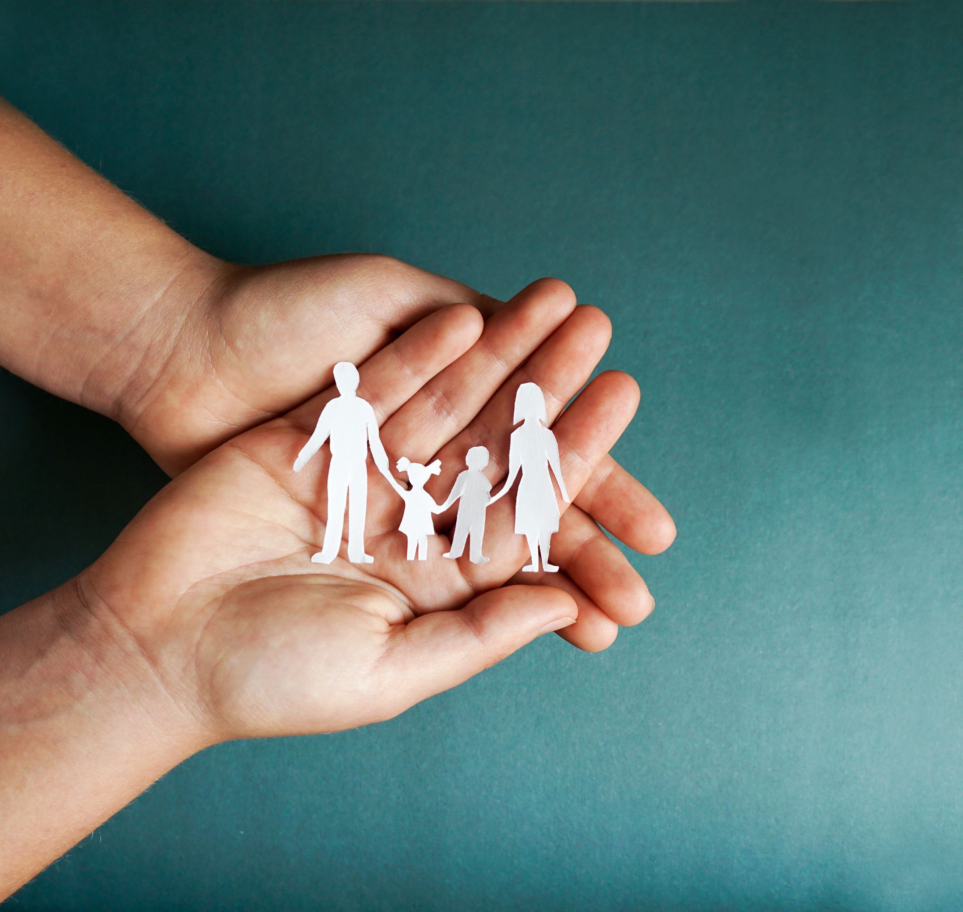 Hands cupping a paper cutout of a family, against a teal background.