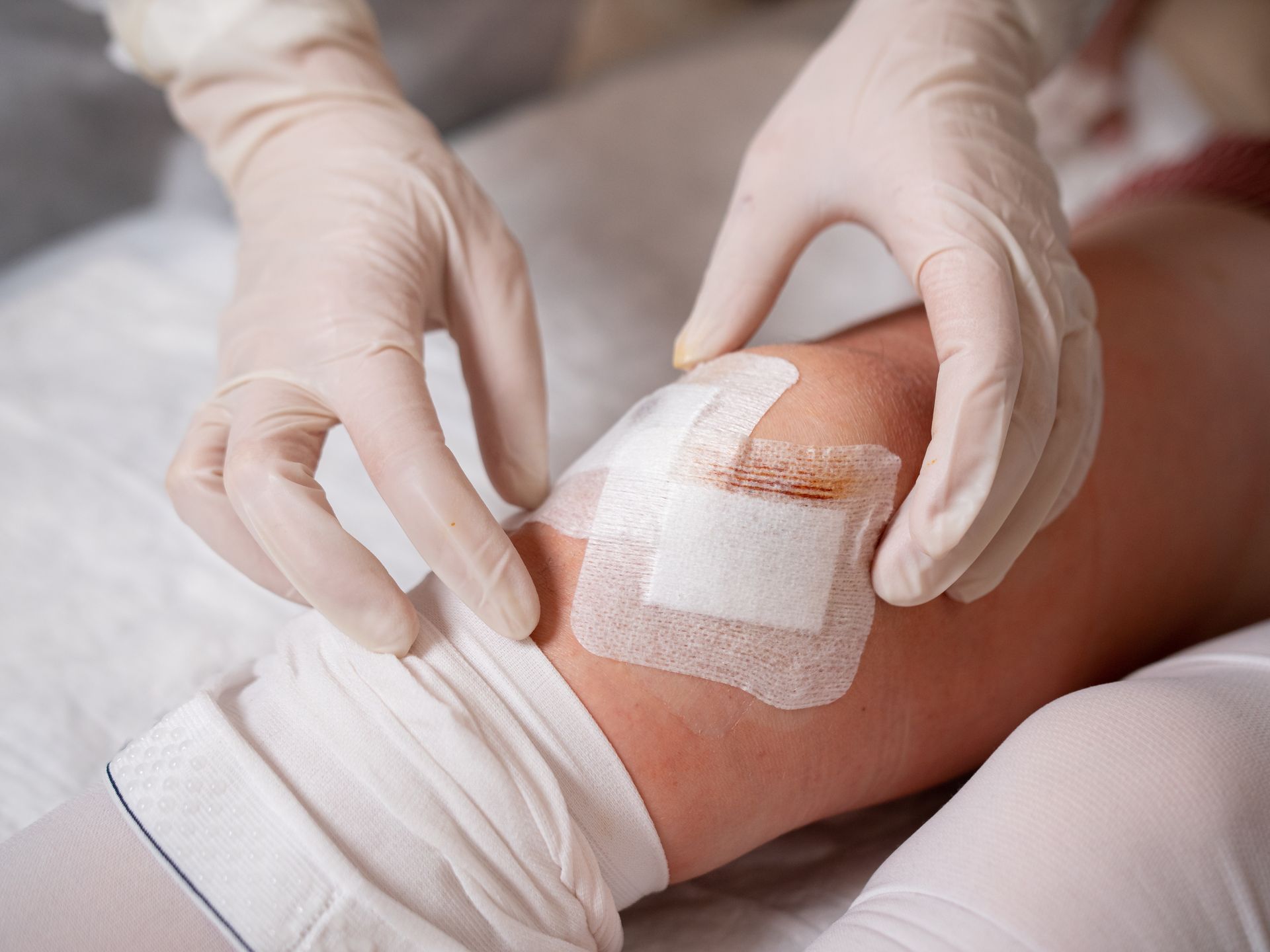 Hands in gloves applying a bandage to a knee.
