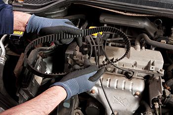 A man wearing gloves is working on the engine of a car.