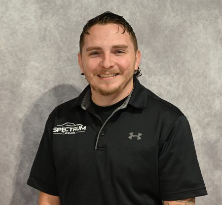 Smiling person in a black polo shirt standing against a gray wall