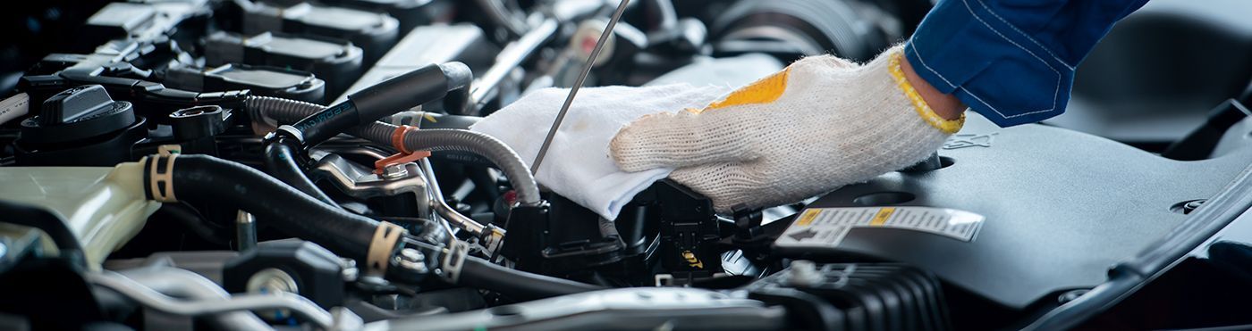 A gloved hand holds a cloth while performing maintenance on an open car engine.